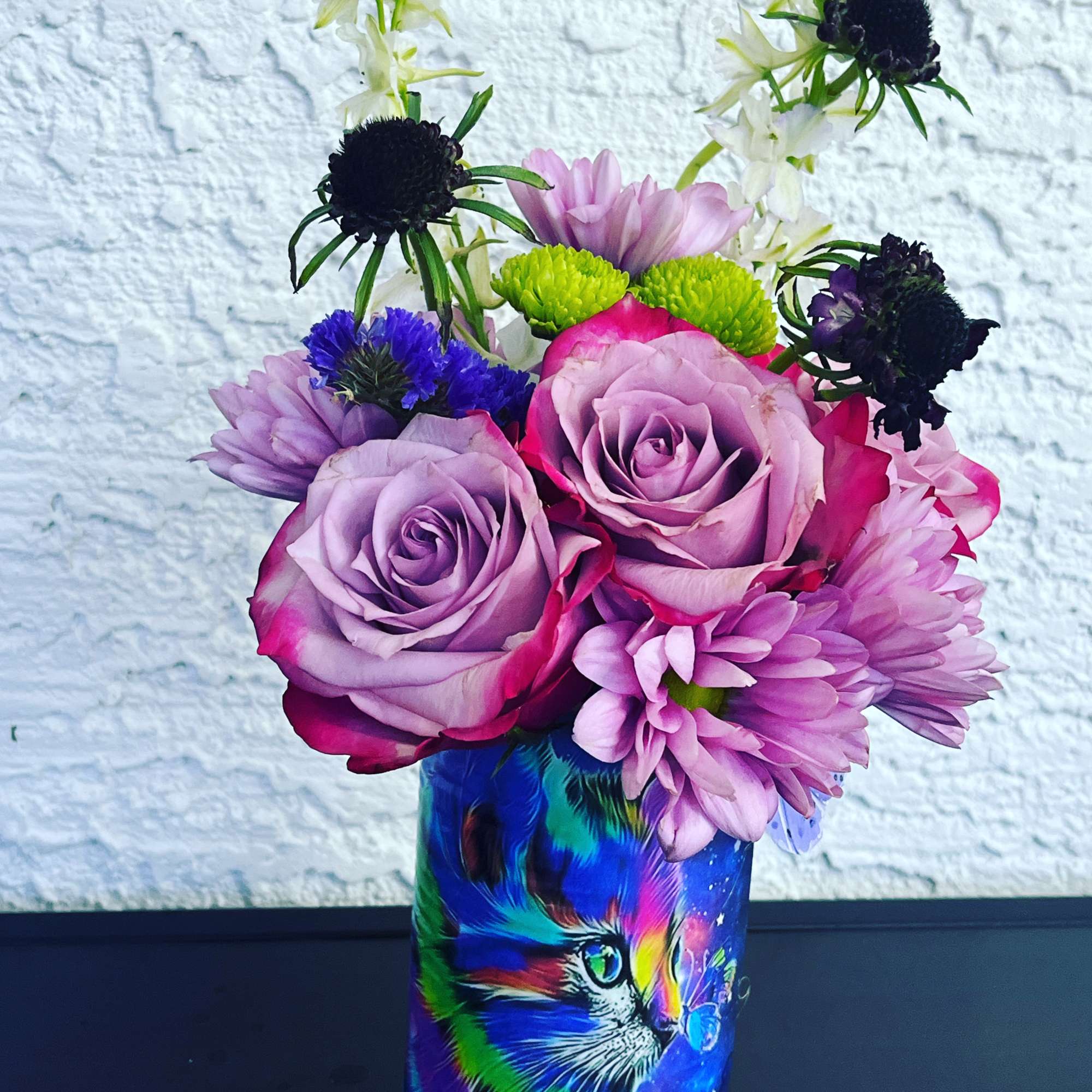 Bouquet of purple roses and mixed blooms in a colorful cat-print vase