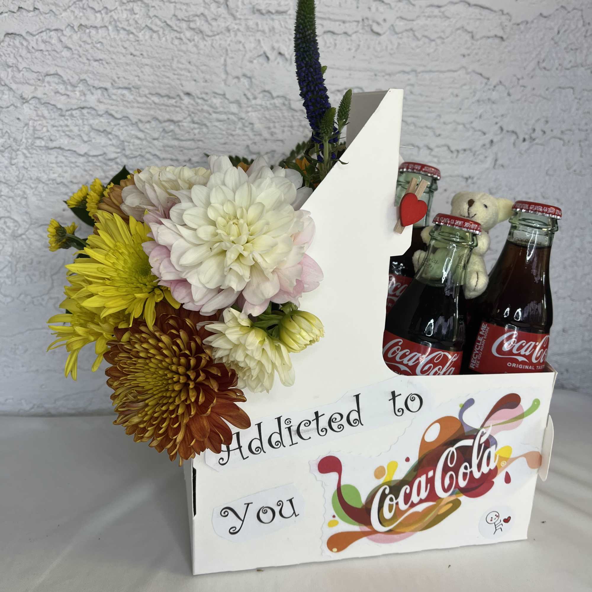 Flower arrangement in a Coca-Cola gift box with small soda bottles and a teddy bear