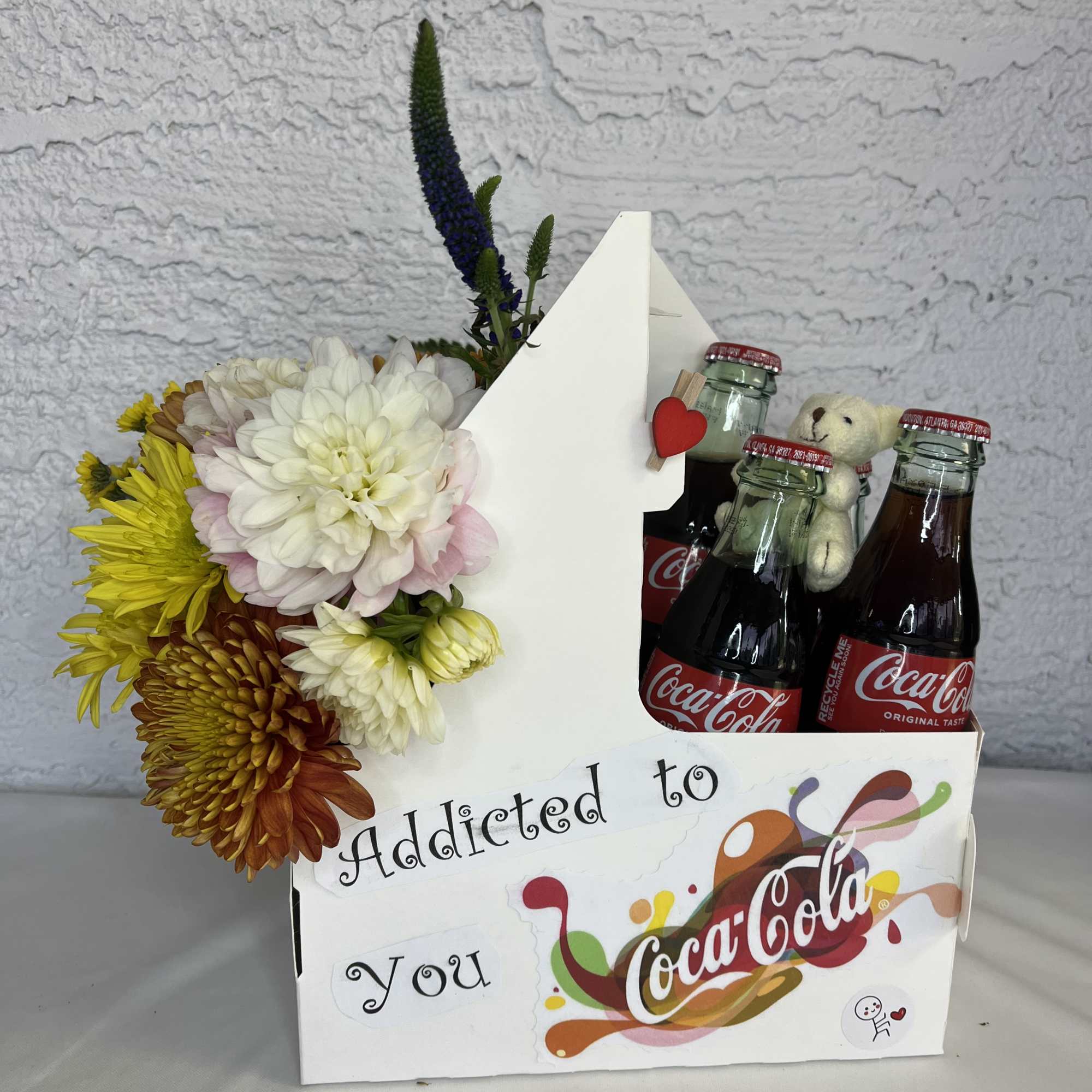 Flower arrangement with Coca-Cola bottles and a small teddy bear in a gift box