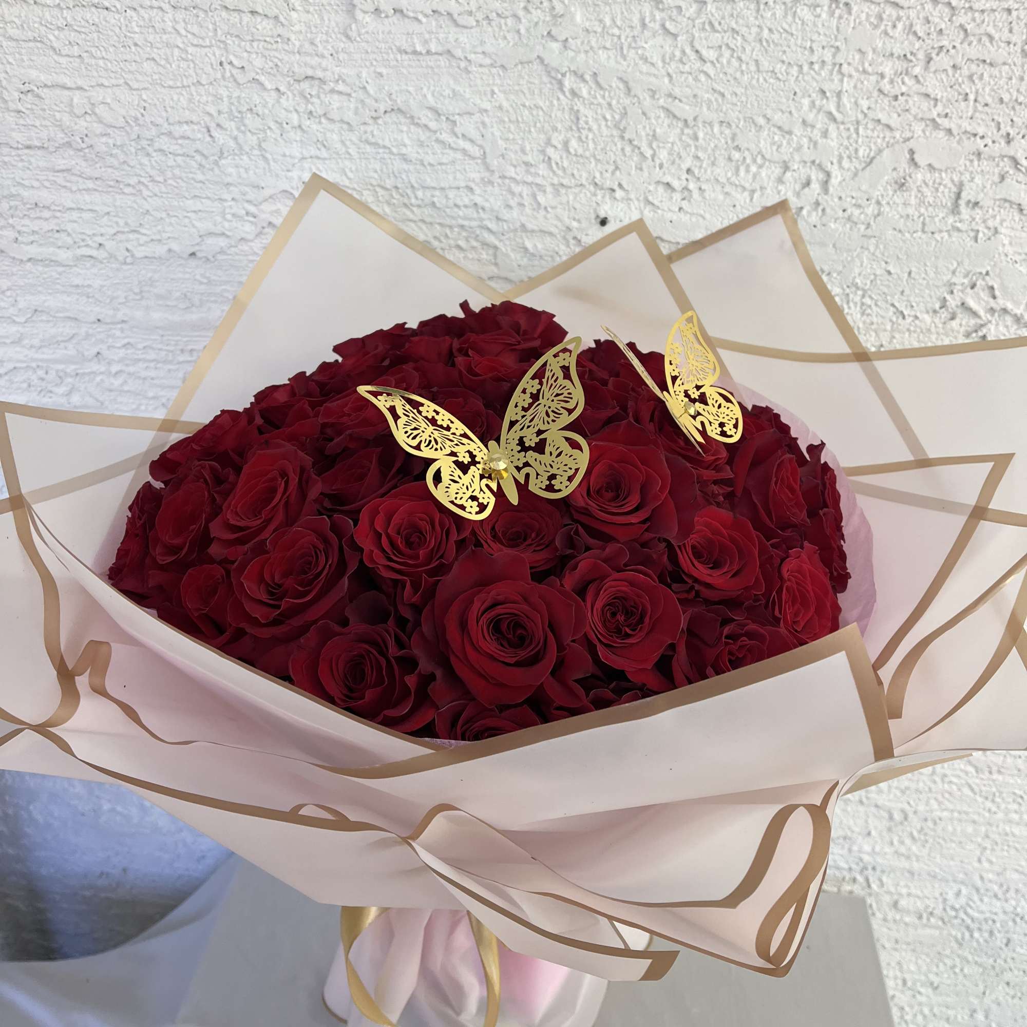Bouquet of deep red roses wrapped in pale pink paper with gold butterfly accents