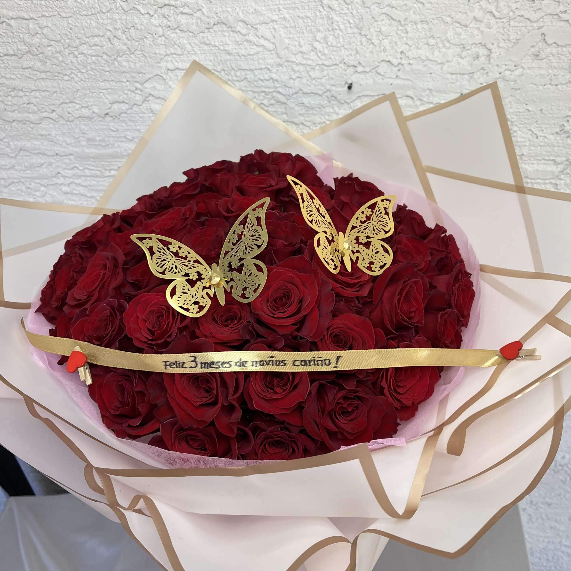 Bouquet of red roses wrapped in cream paper with gold trim and butterfly picks