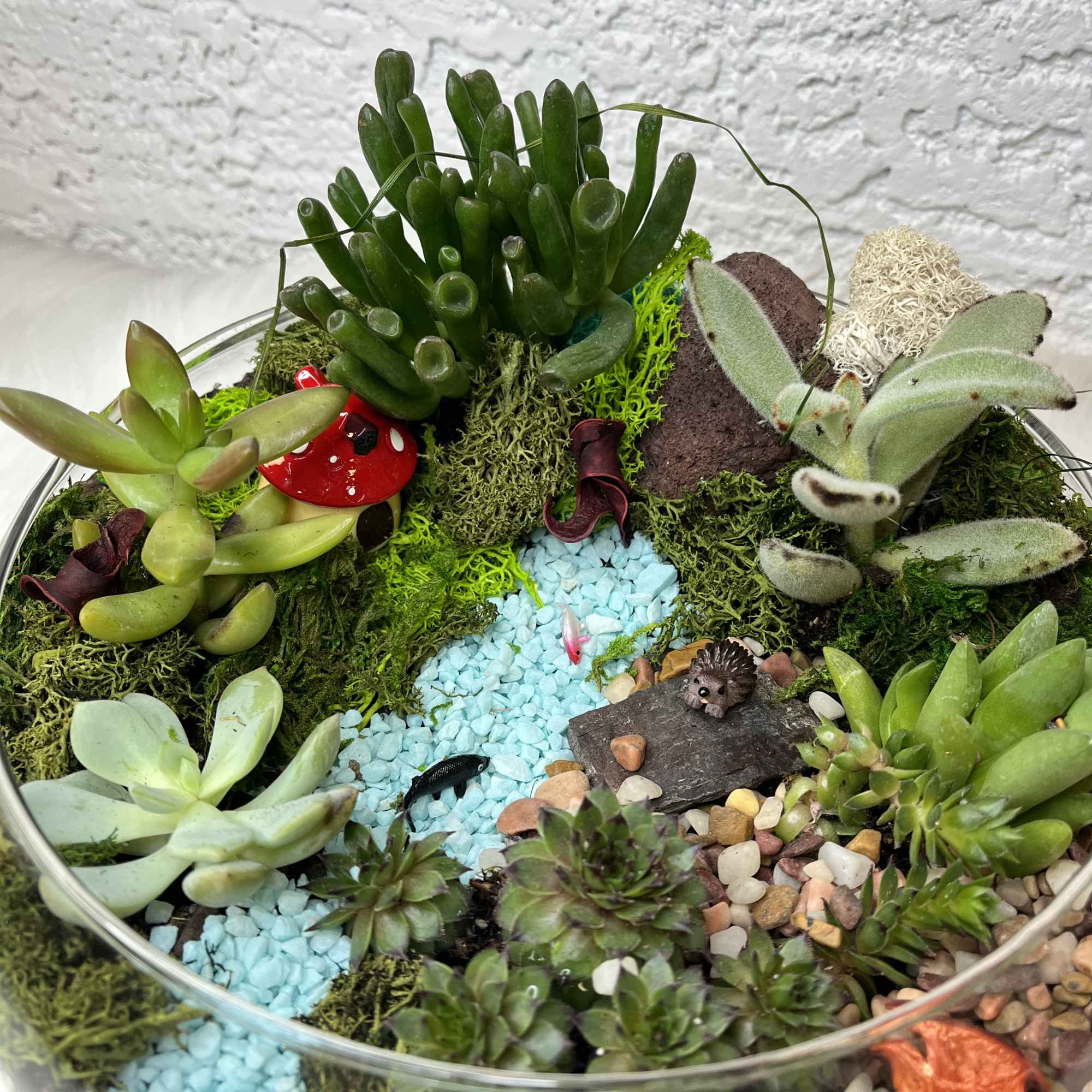 Succulent terrarium in a glass bowl with decorative pebbles and small figurines