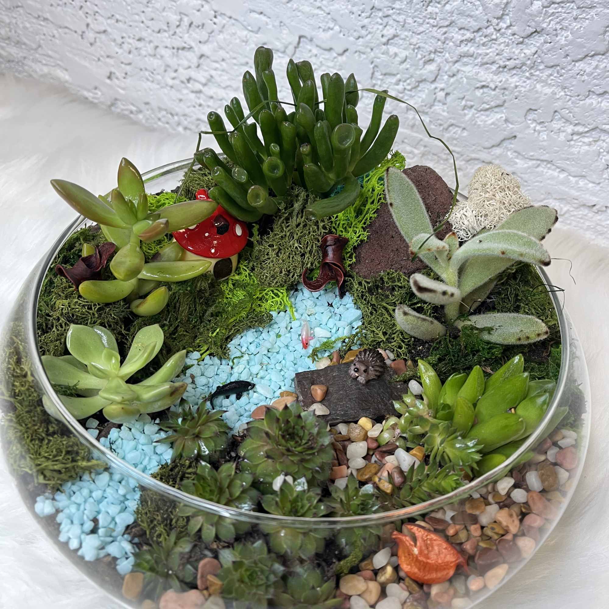 Glass bowl terrarium with assorted succulents, pebbles, and small decorative figures