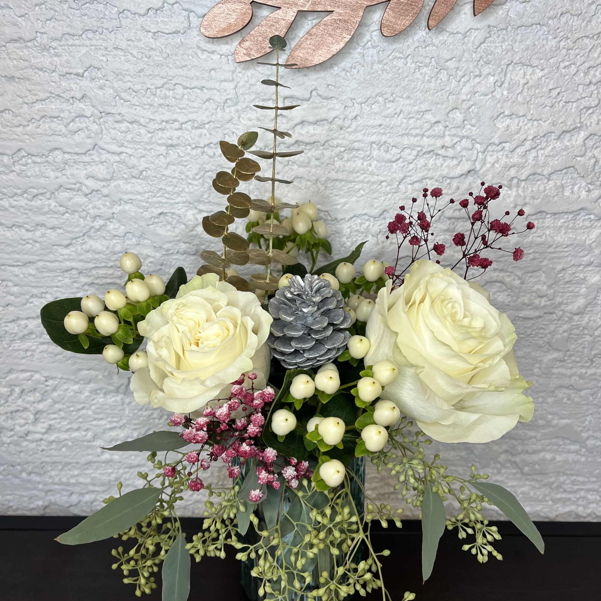 White roses in a teal vase with pink filler flowers and silver pinecone decor