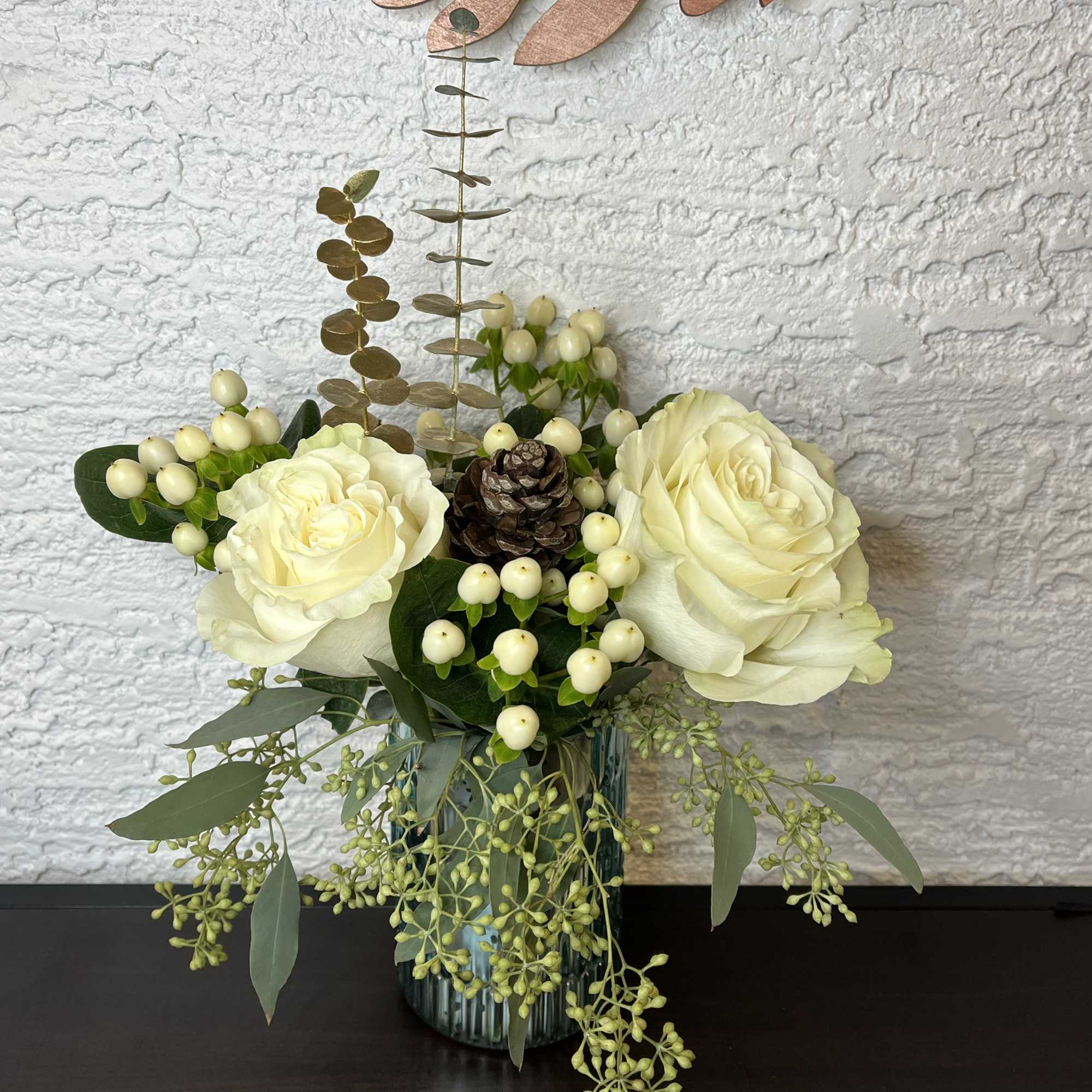 White roses in a glass vase with berries and greenery