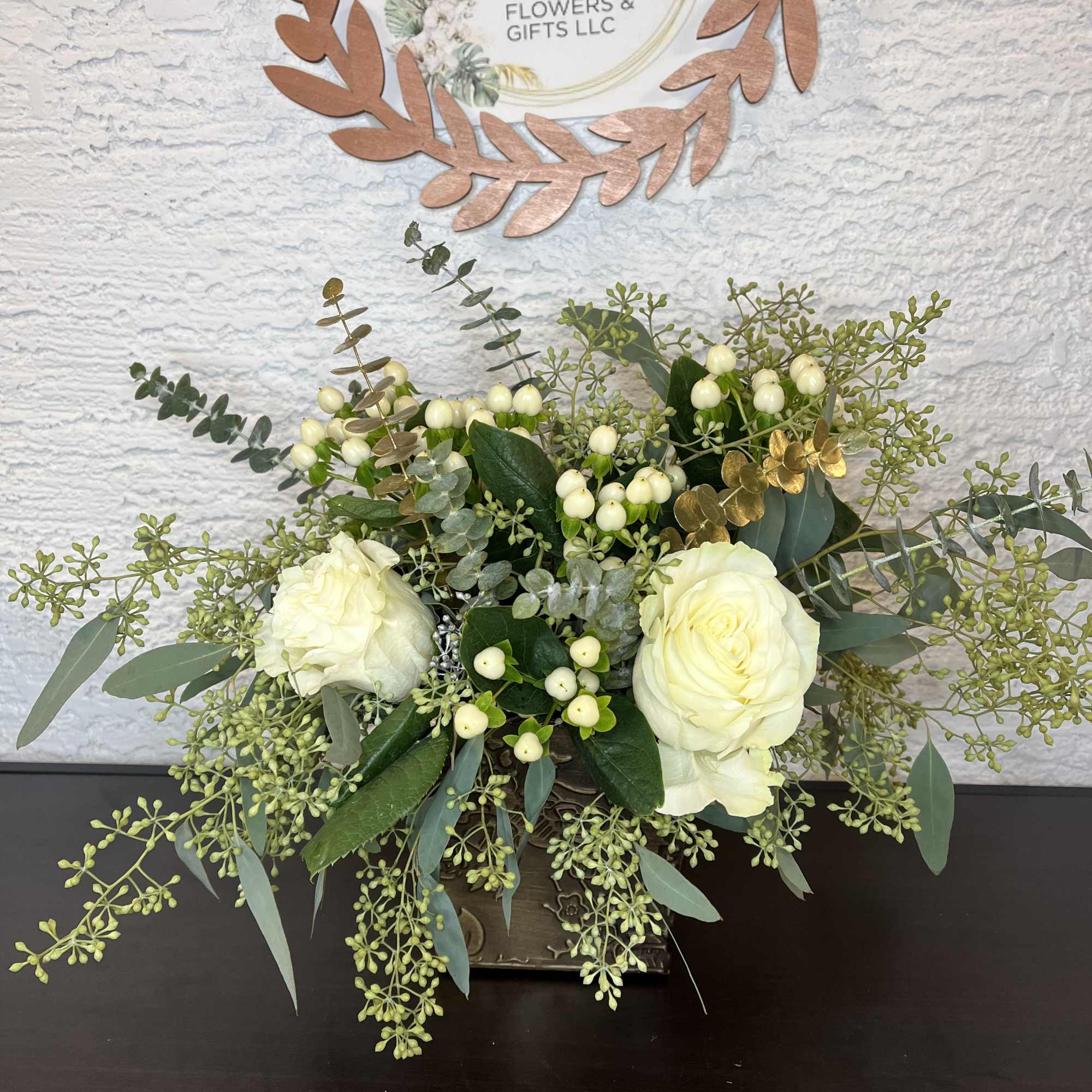 White roses in a low arrangement with eucalyptus and berry accents