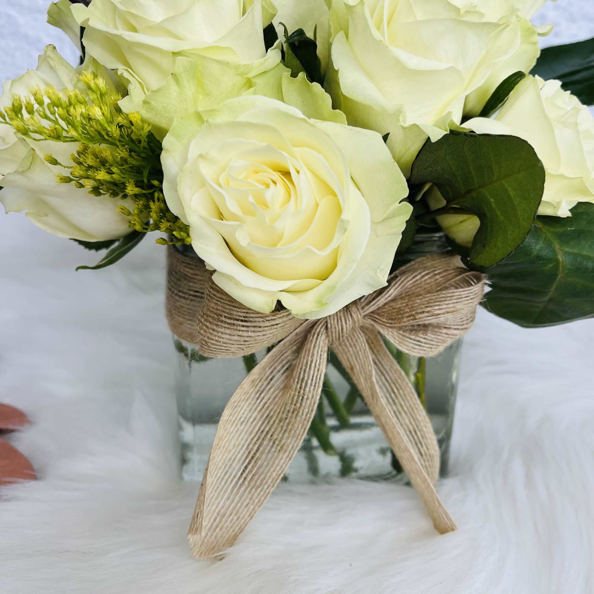 White roses arranged in a glass vase with a burlap bow