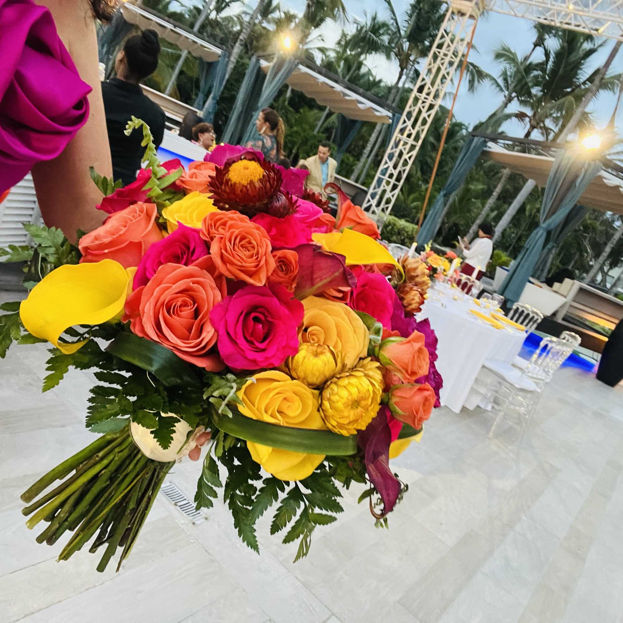 Bright bouquet of roses and calla lilies held at an outdoor event.