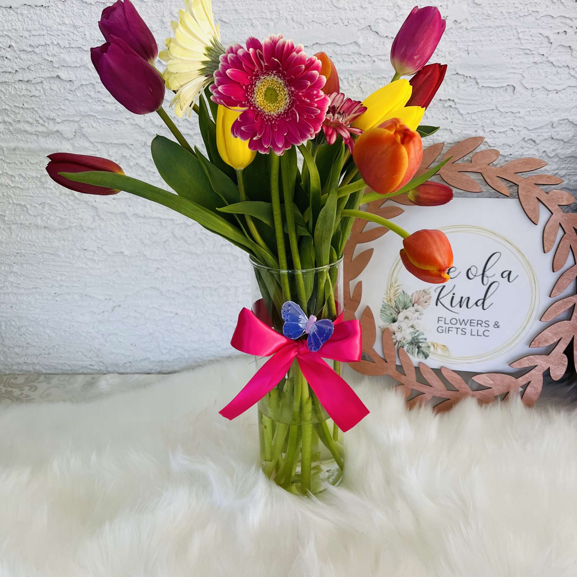 Colorful tulip and gerbera bouquet in a clear glass vase with a pink ribbon