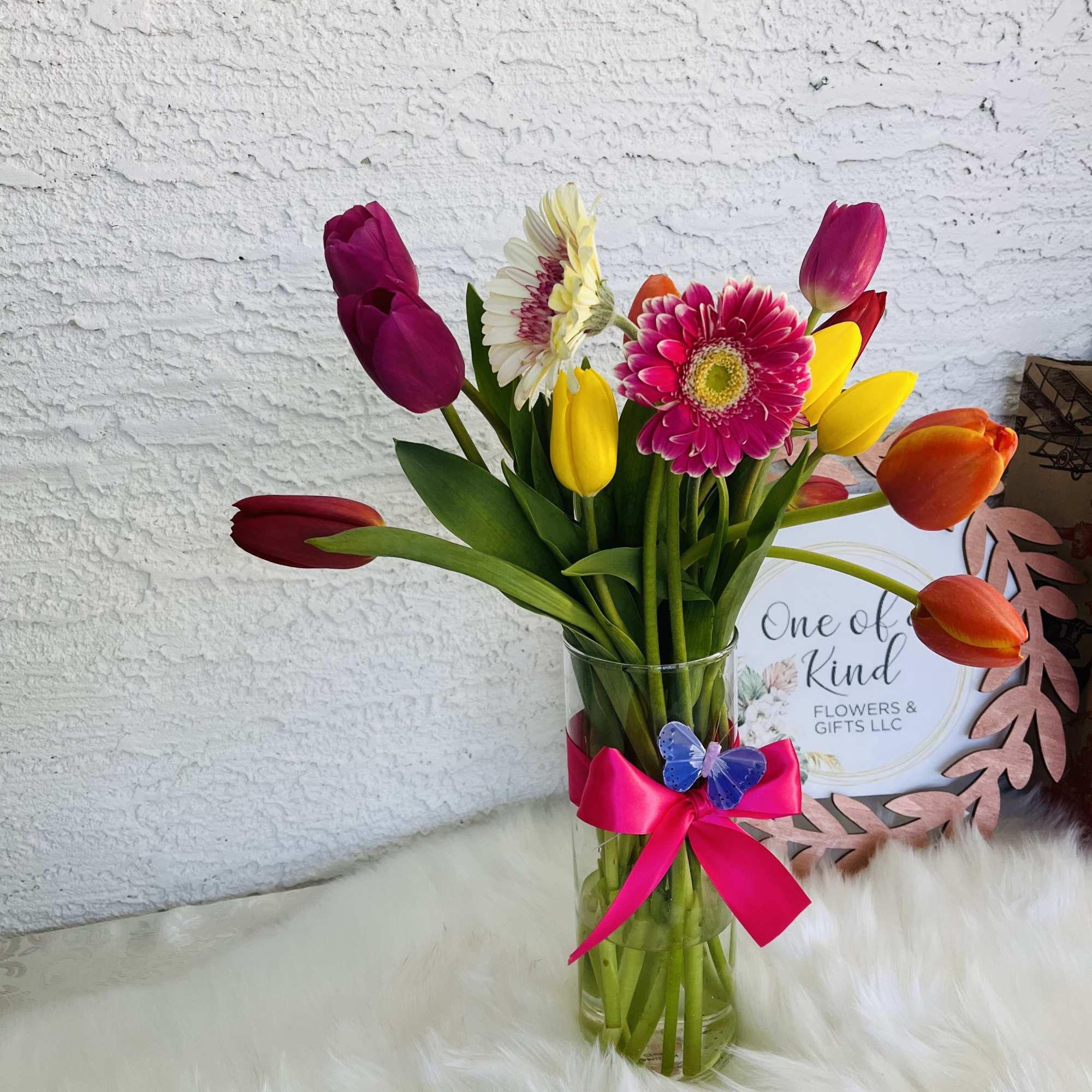 Mixed tulips and gerbera daisies in a glass vase with a pink ribbon
