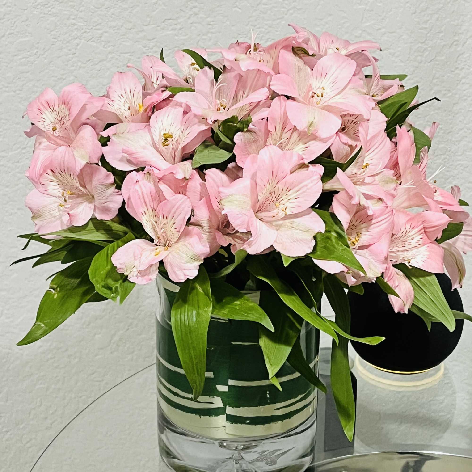 Pink alstroemeria arrangement in a clear glass cylinder vase on a glass table