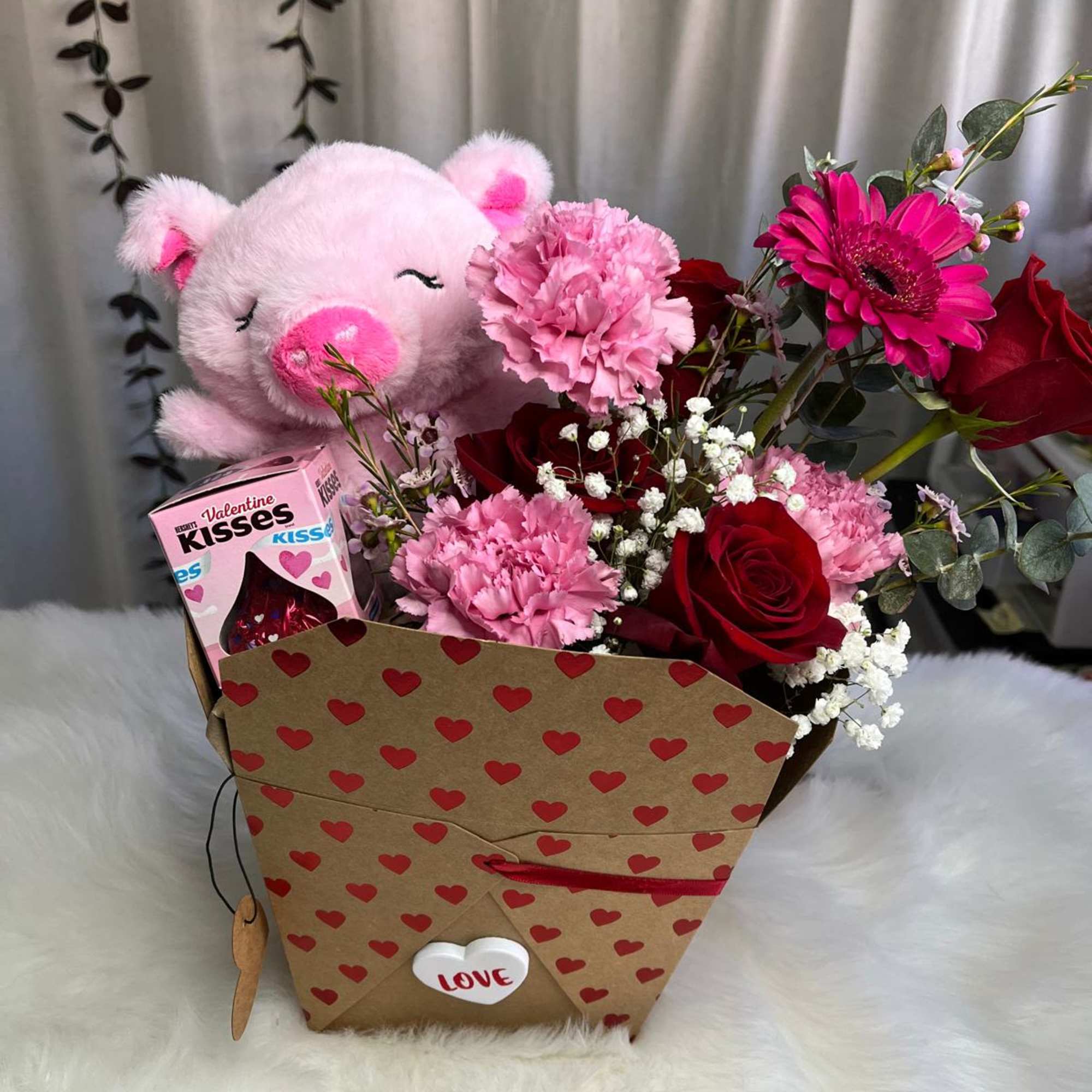 Pink teddy bear and chocolates with a red and pink flower arrangement in a heart-patterned box