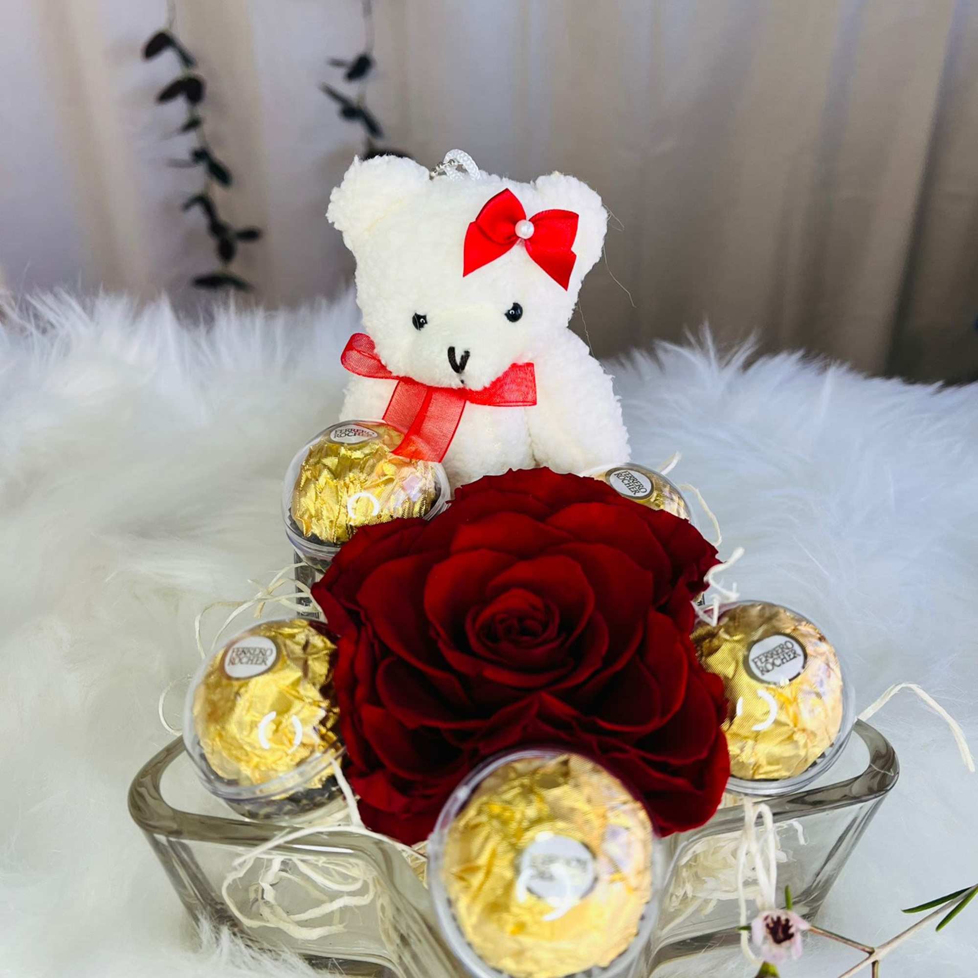 Red rose arrangement with a teddy bear and gold-wrapped chocolates in a glass bowl