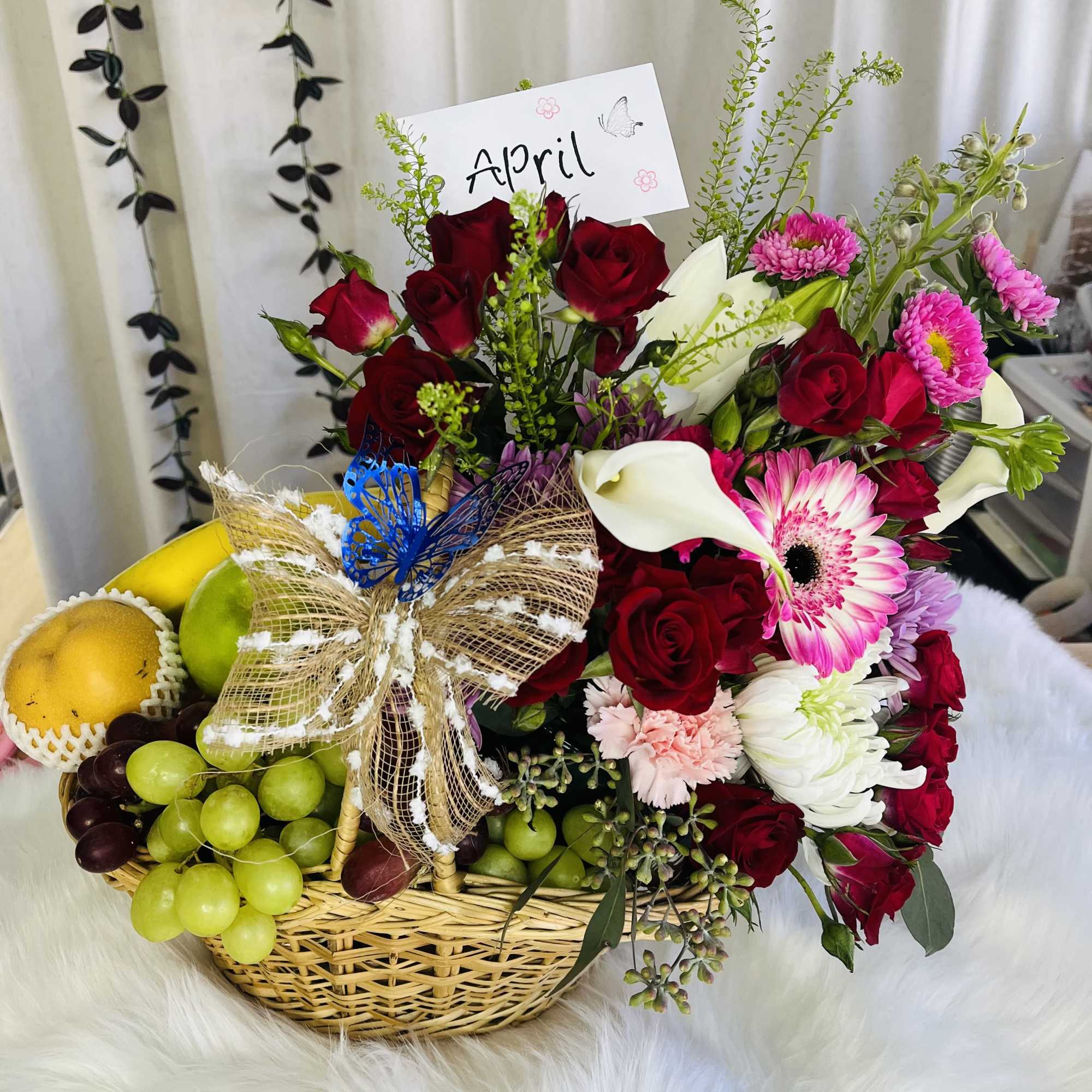 Basket of red roses, pink daisies, and fruit with a butterfly bow