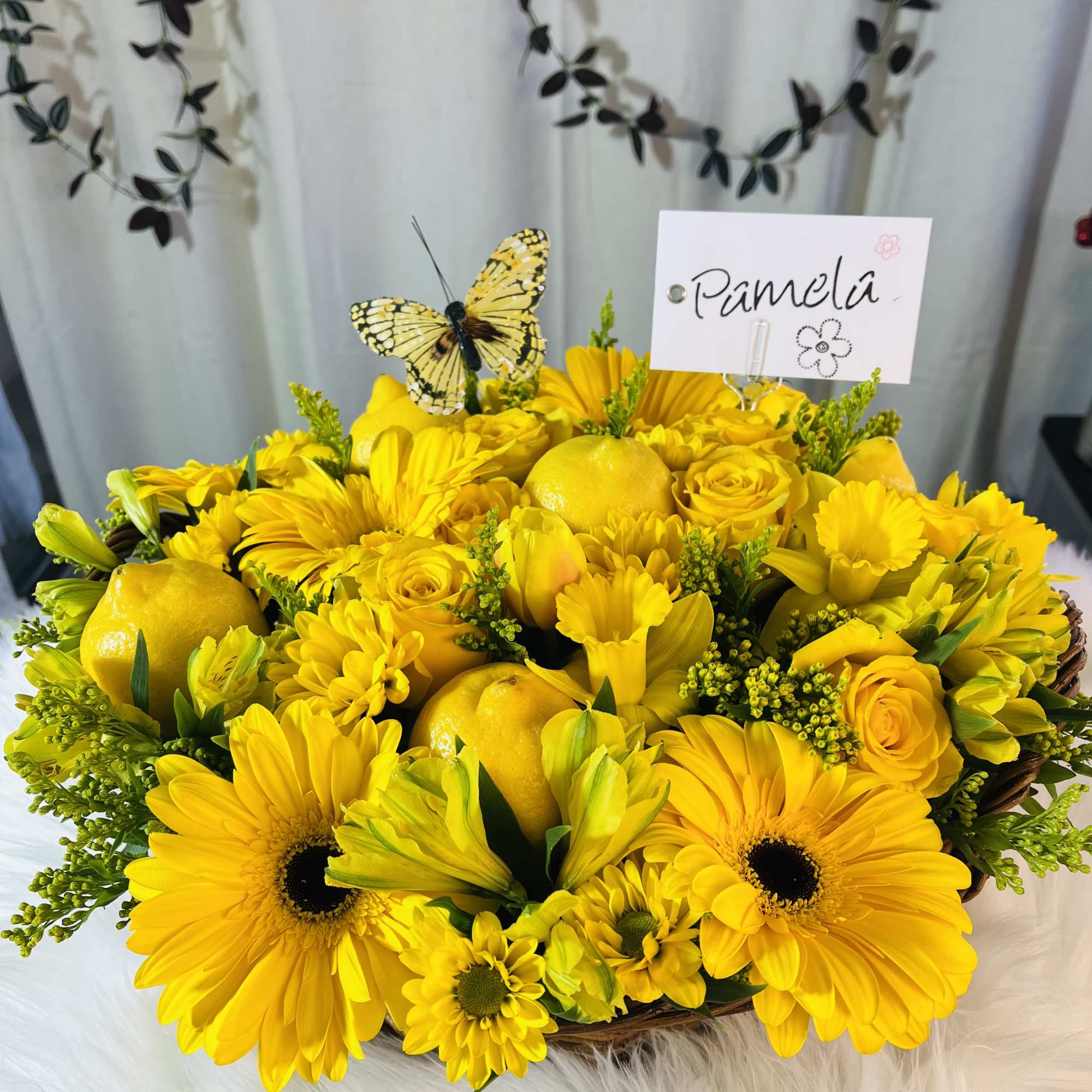 Low basket of bright yellow flowers with lemons, a small butterfly pick, and a name card reading Pamela