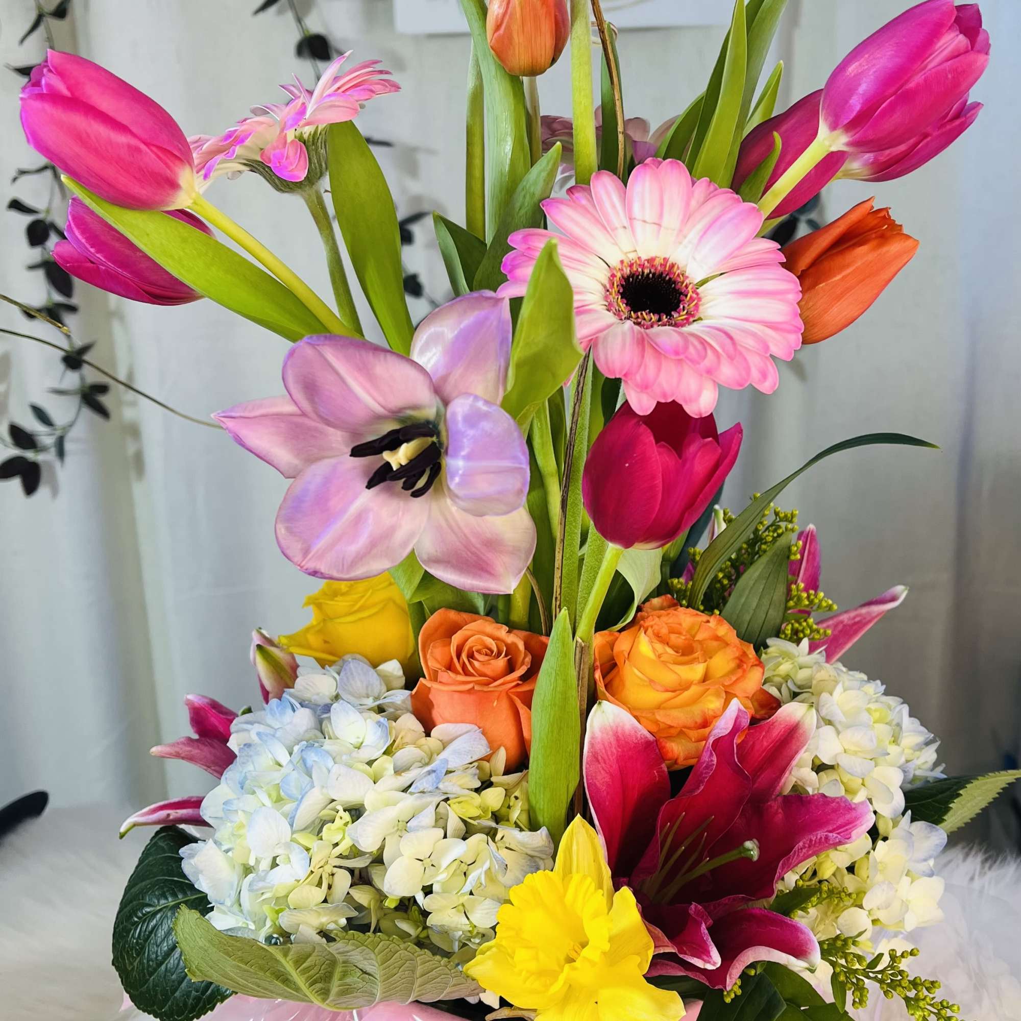 Colorful mixed bouquet in a pink hatbox with tulips, gerberas, roses, and hydrangeas