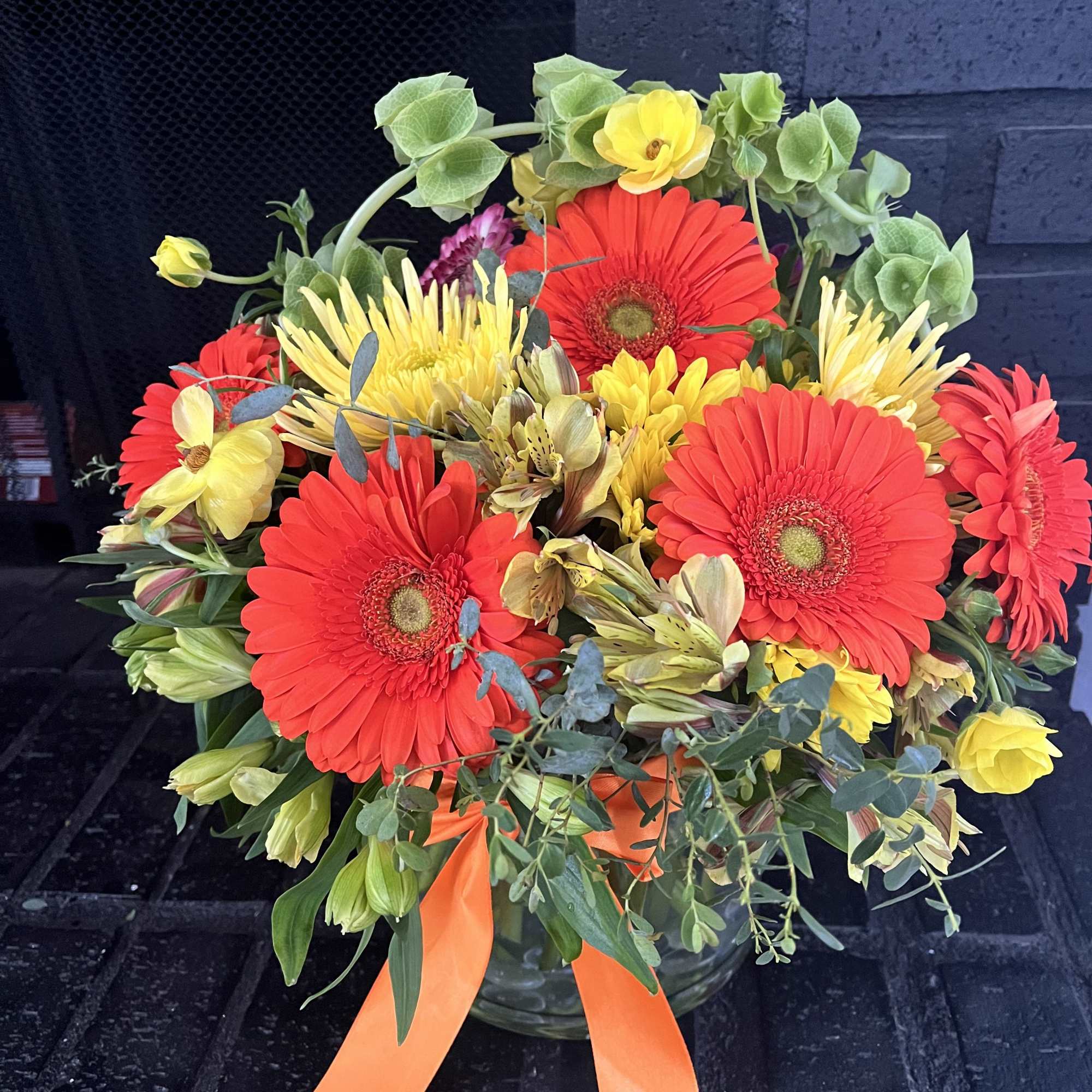 Bright gerbera daisy bouquet in a glass vase with orange ribbon