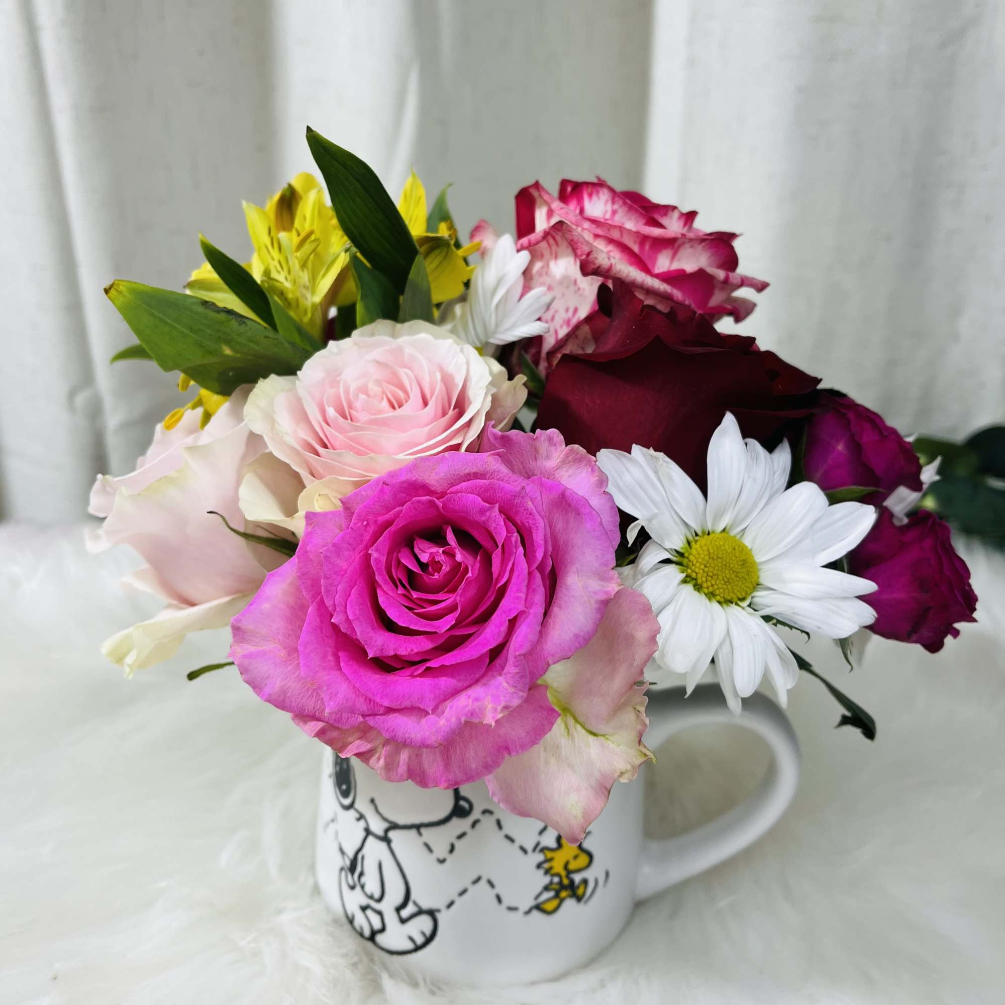 Mixed roses and daisies arranged in a Snoopy mug