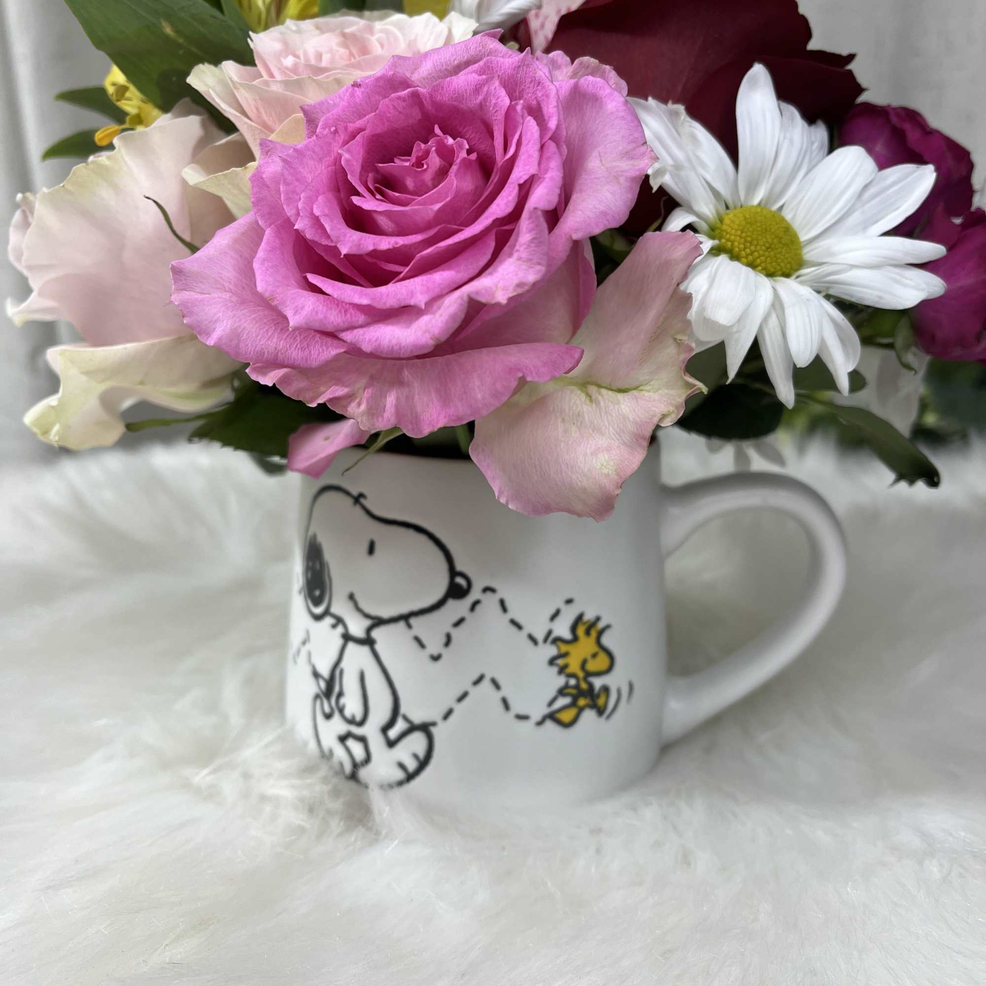 Pink and burgundy roses with white daisies in a Snoopy mug