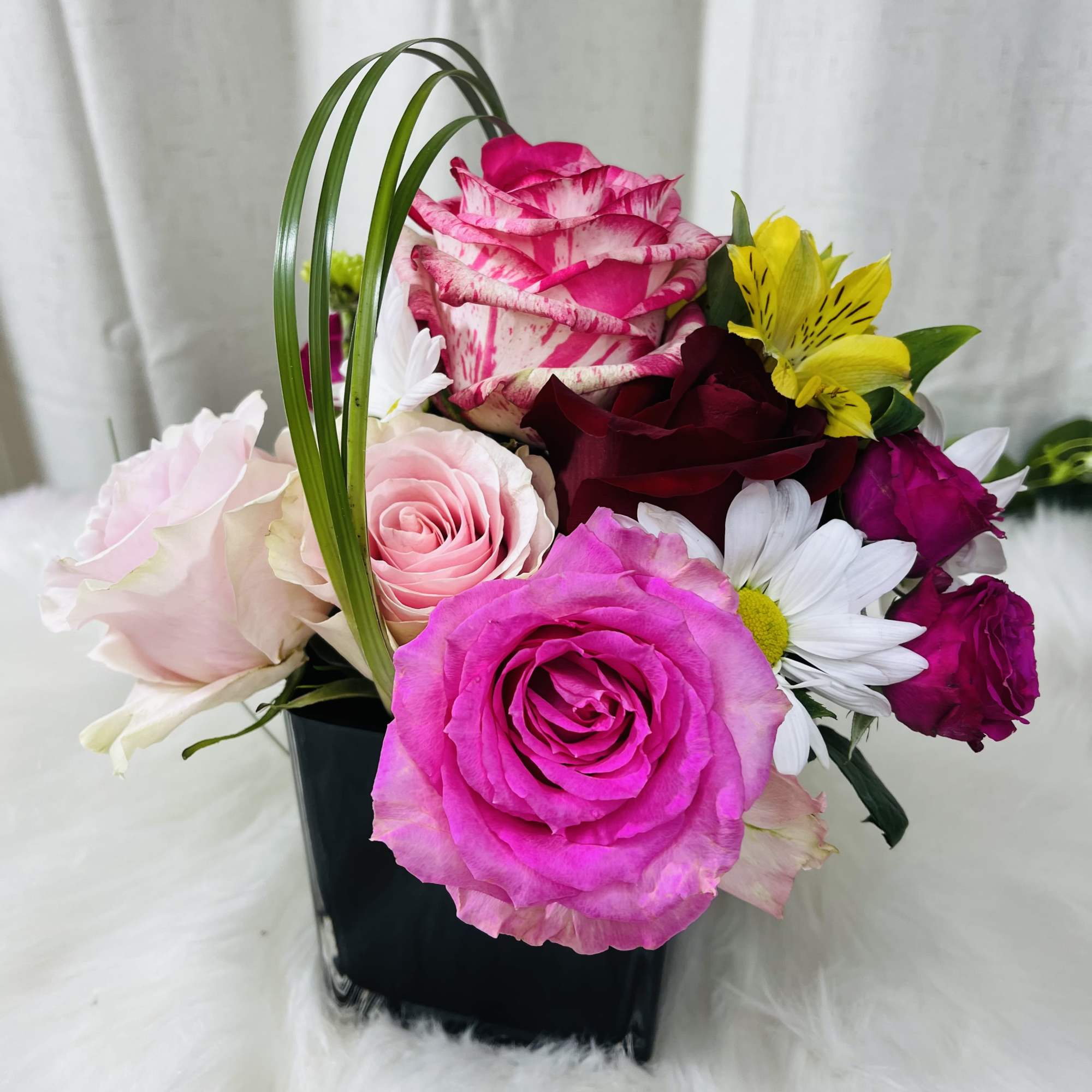 Mixed bouquet of pink, white, and yellow flowers in a black vase
