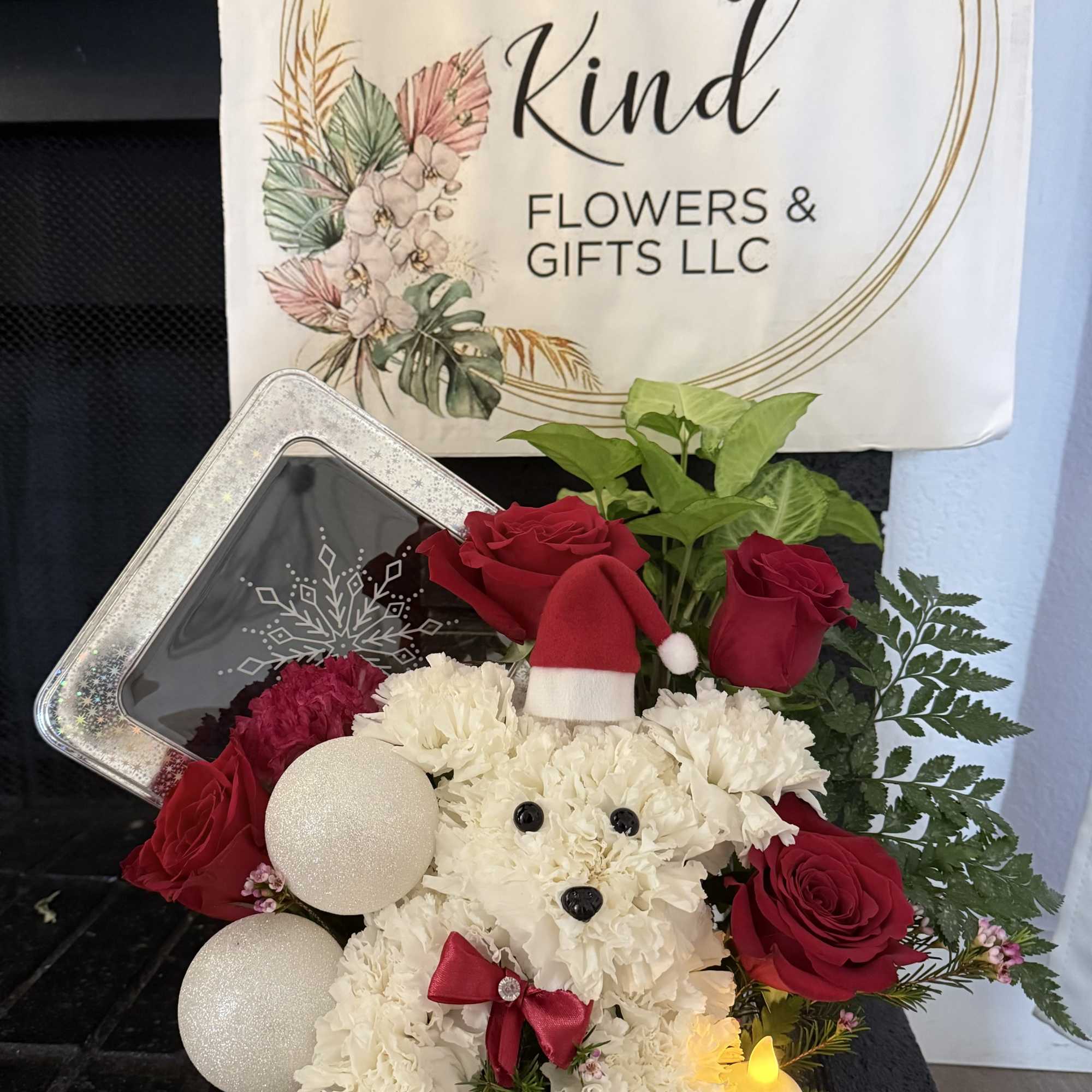 Holiday gift arrangement with white flowers, red roses, and a plush dog in a tin box
