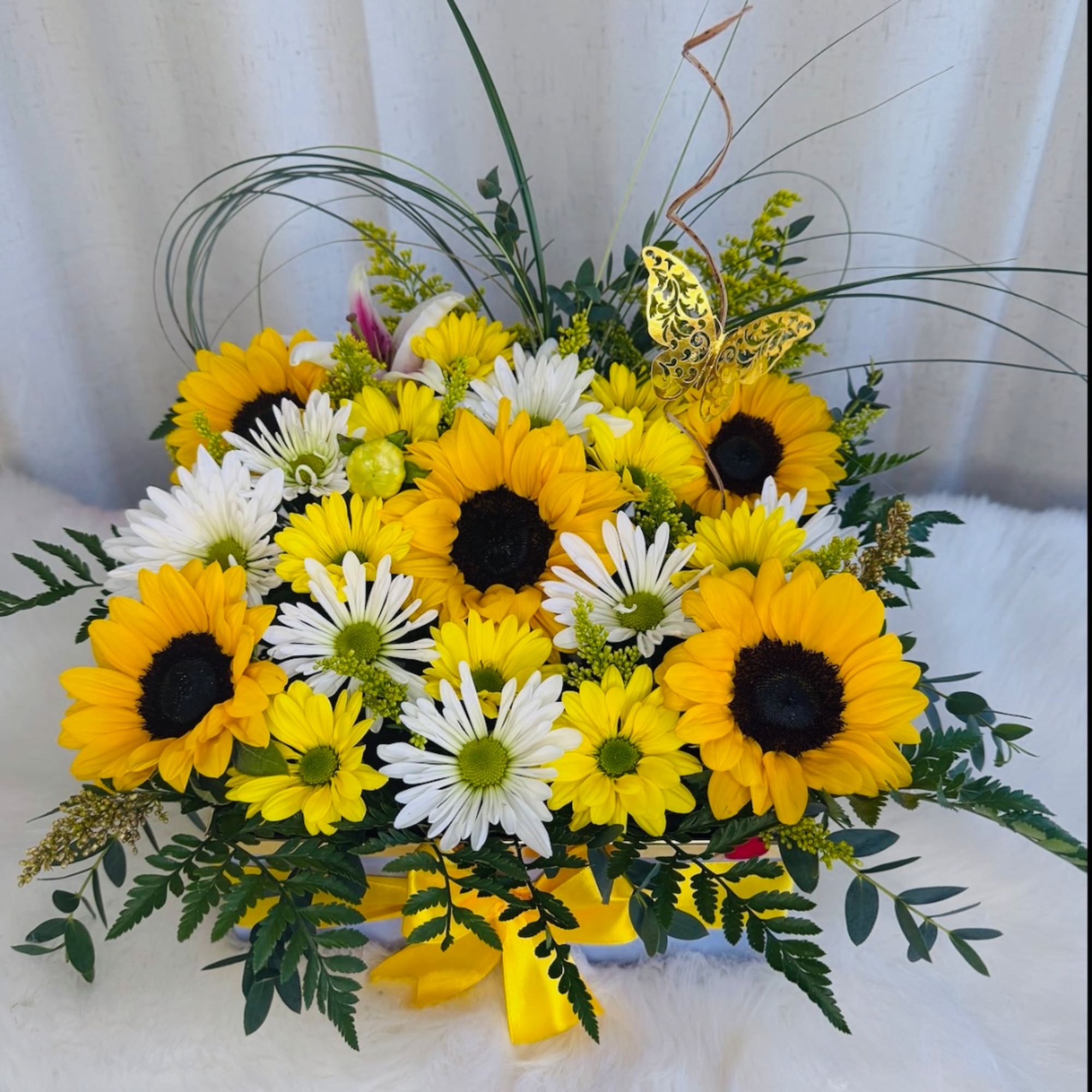 Yellow sunflowers and white daisies arranged in a low bouquet with a yellow ribbon