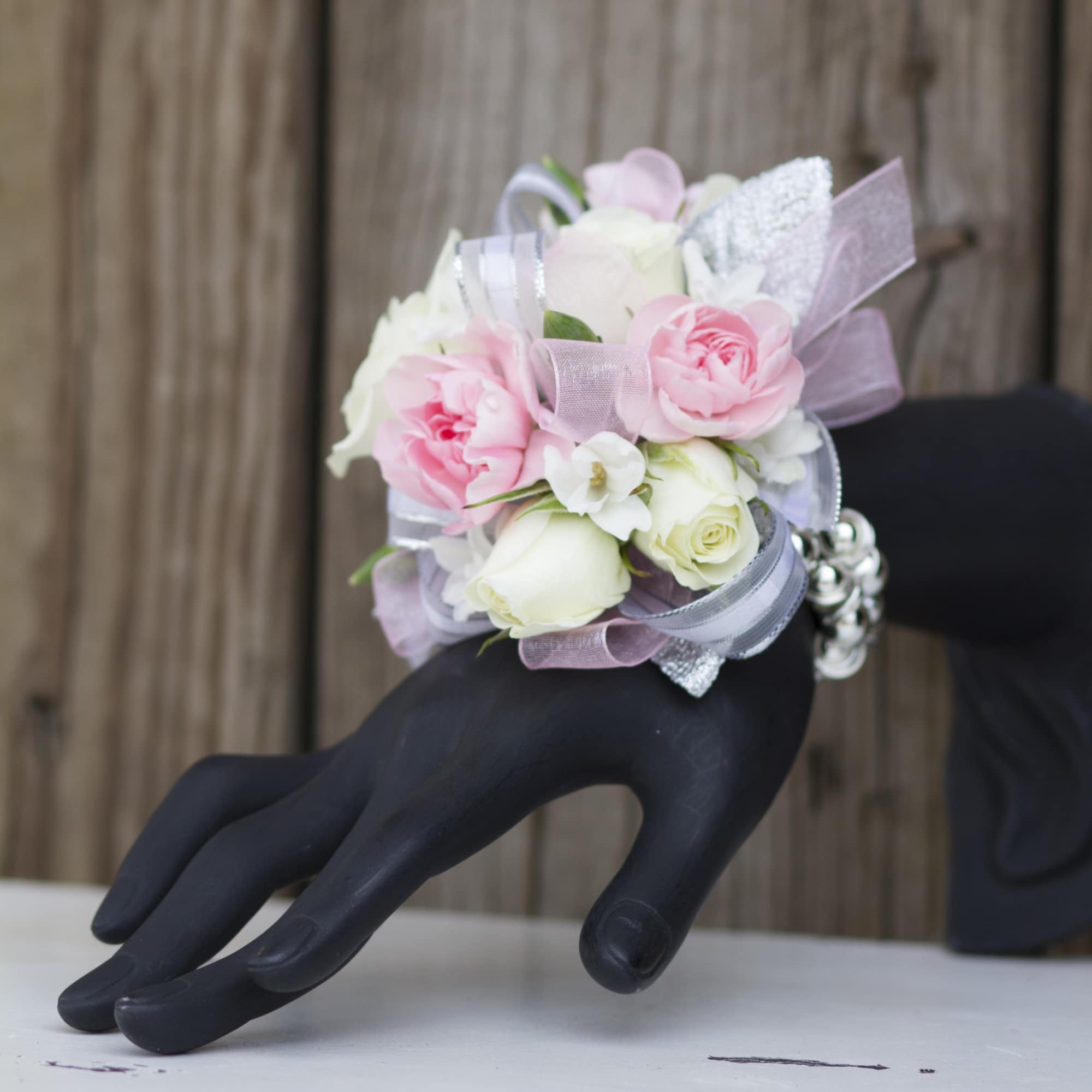 Pink and white rose wrist corsage with ribbons on a black mannequin hand