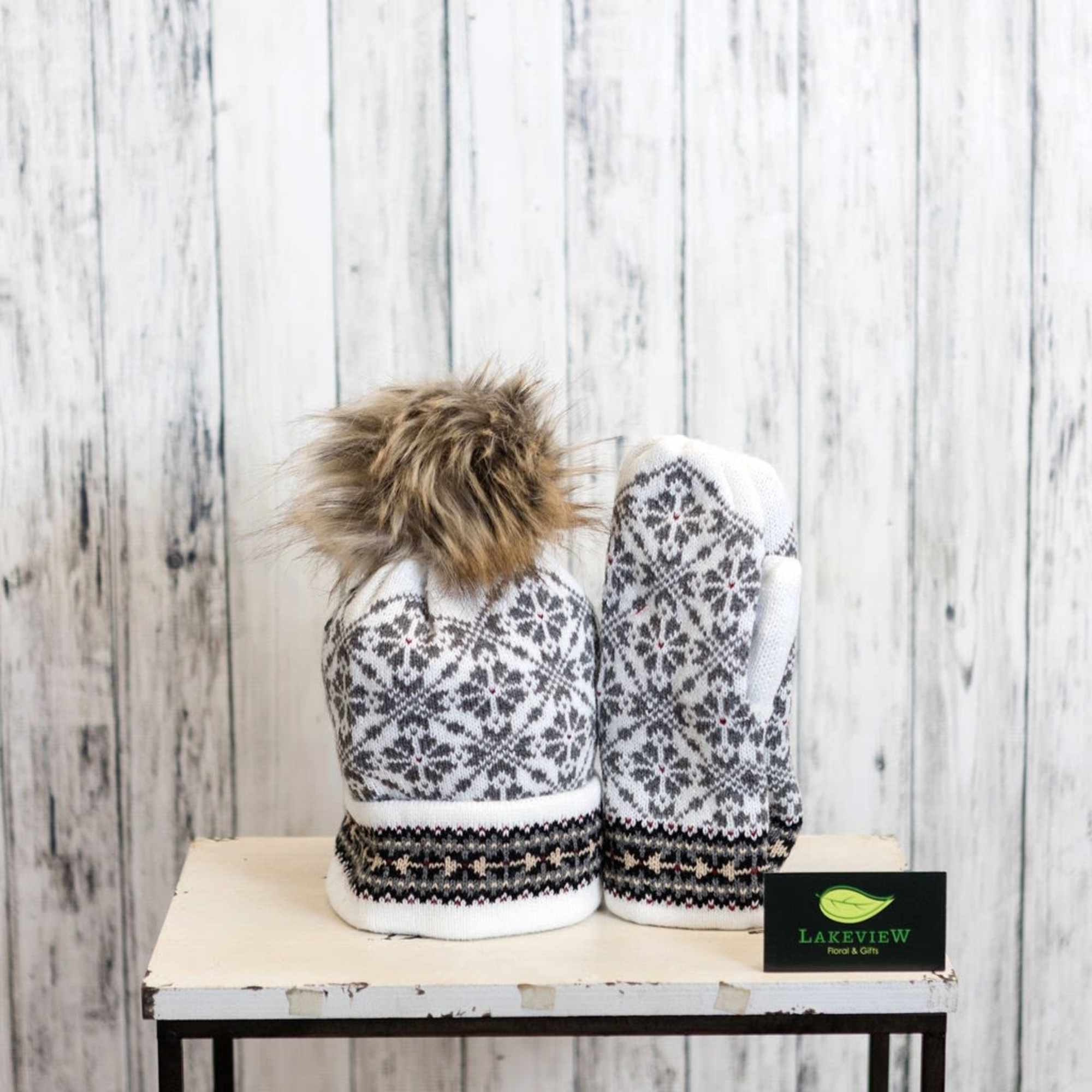 Pair of patterned winter mittens with a fur pom-pom on a small table