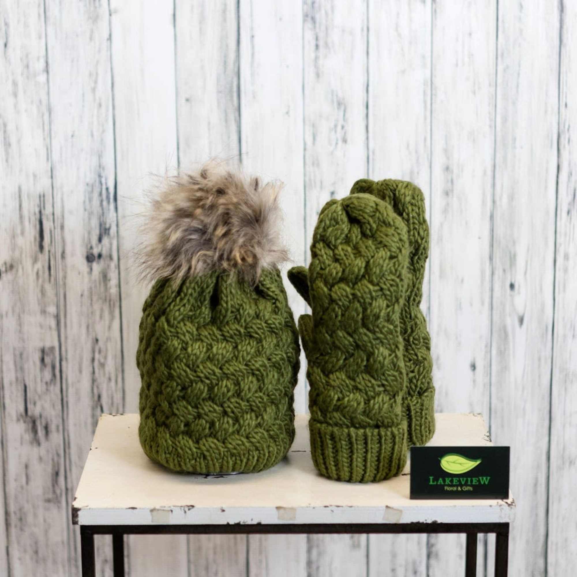 Two green knitted winter accessories with a fur pom-pom on a table