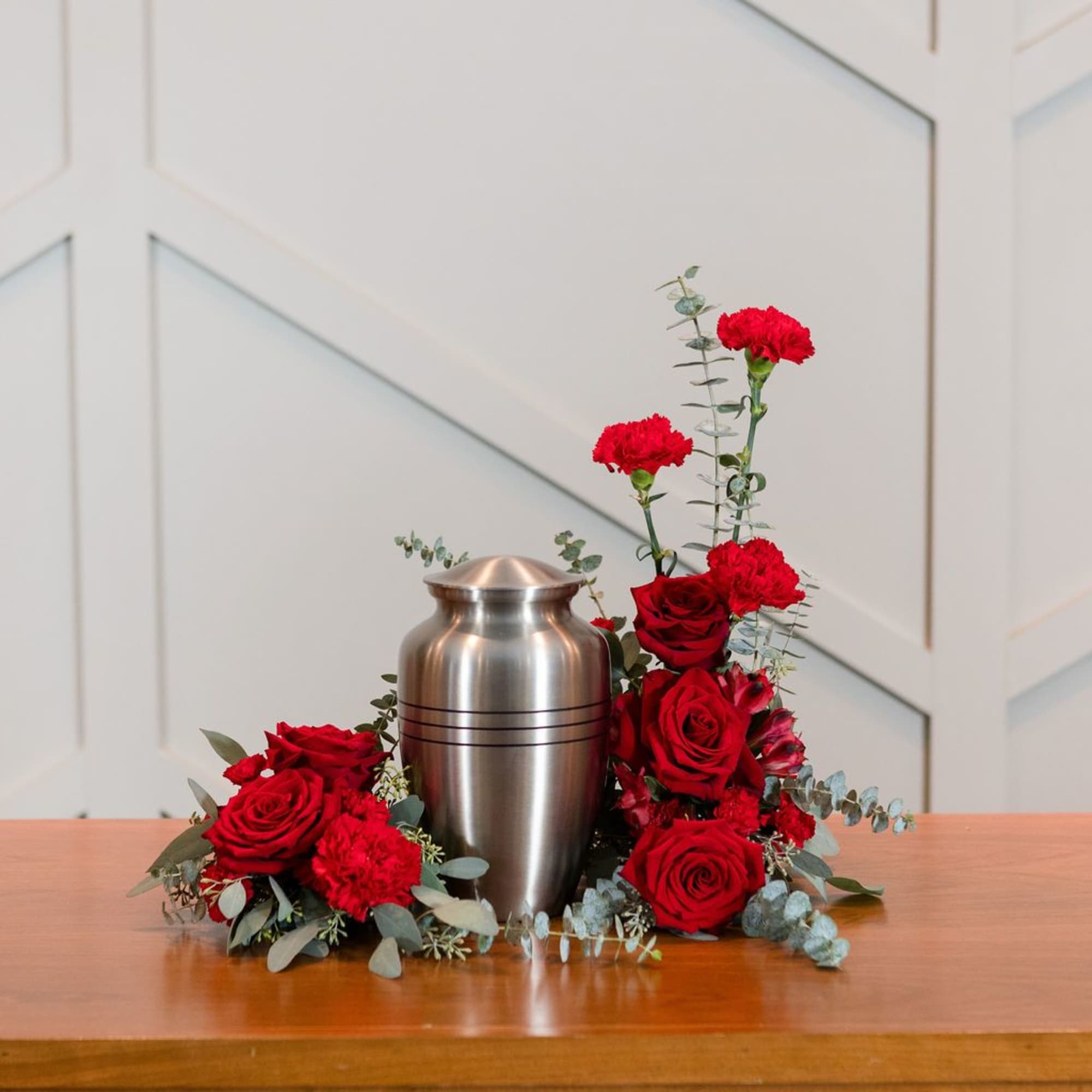 Red roses and carnations arranged around a silver urn