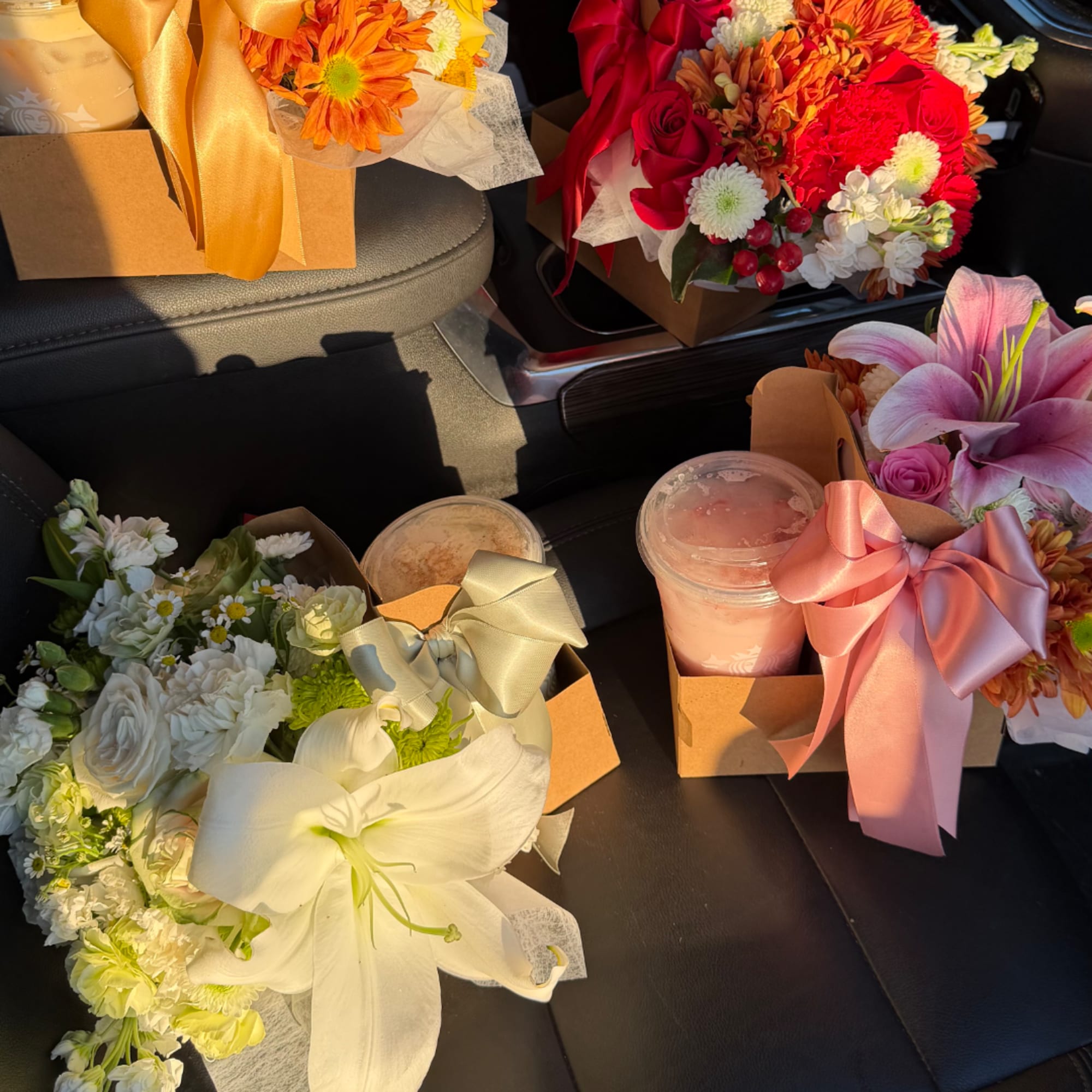 Several boxed flower arrangements with ribbons and drinks on a car seat