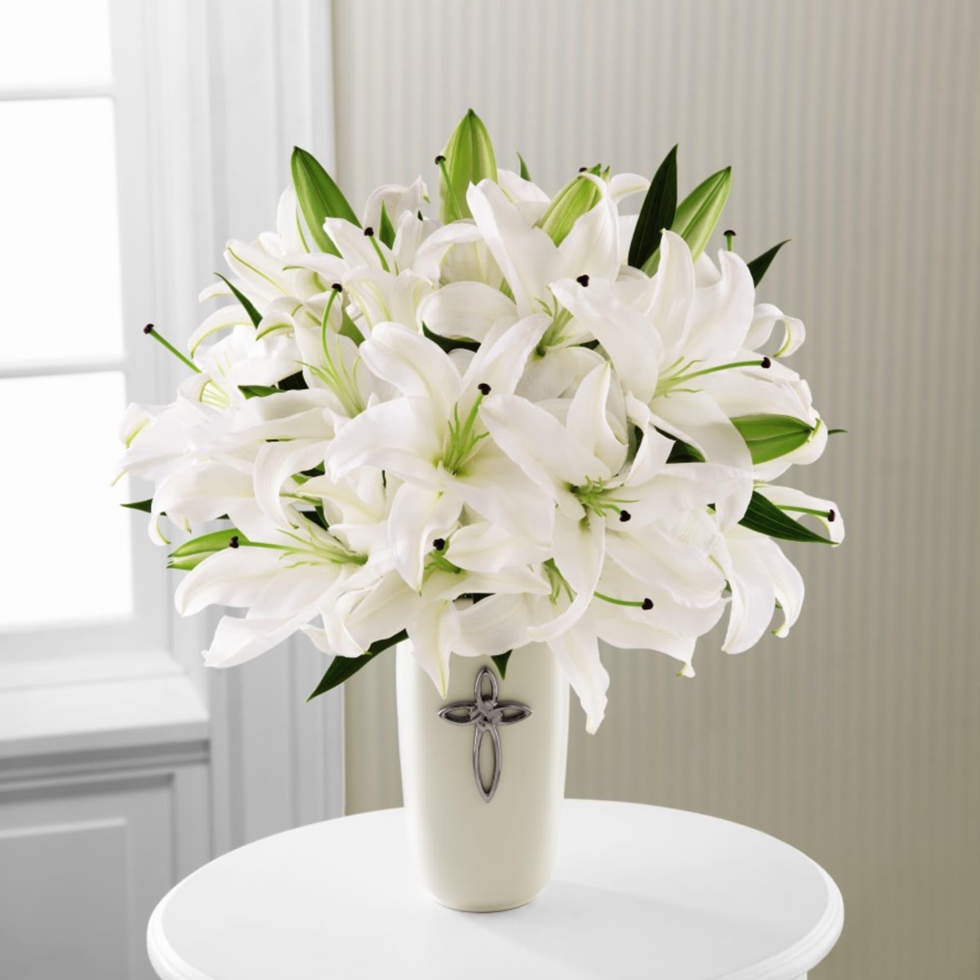 White lilies arranged in a tall vase with a cross emblem