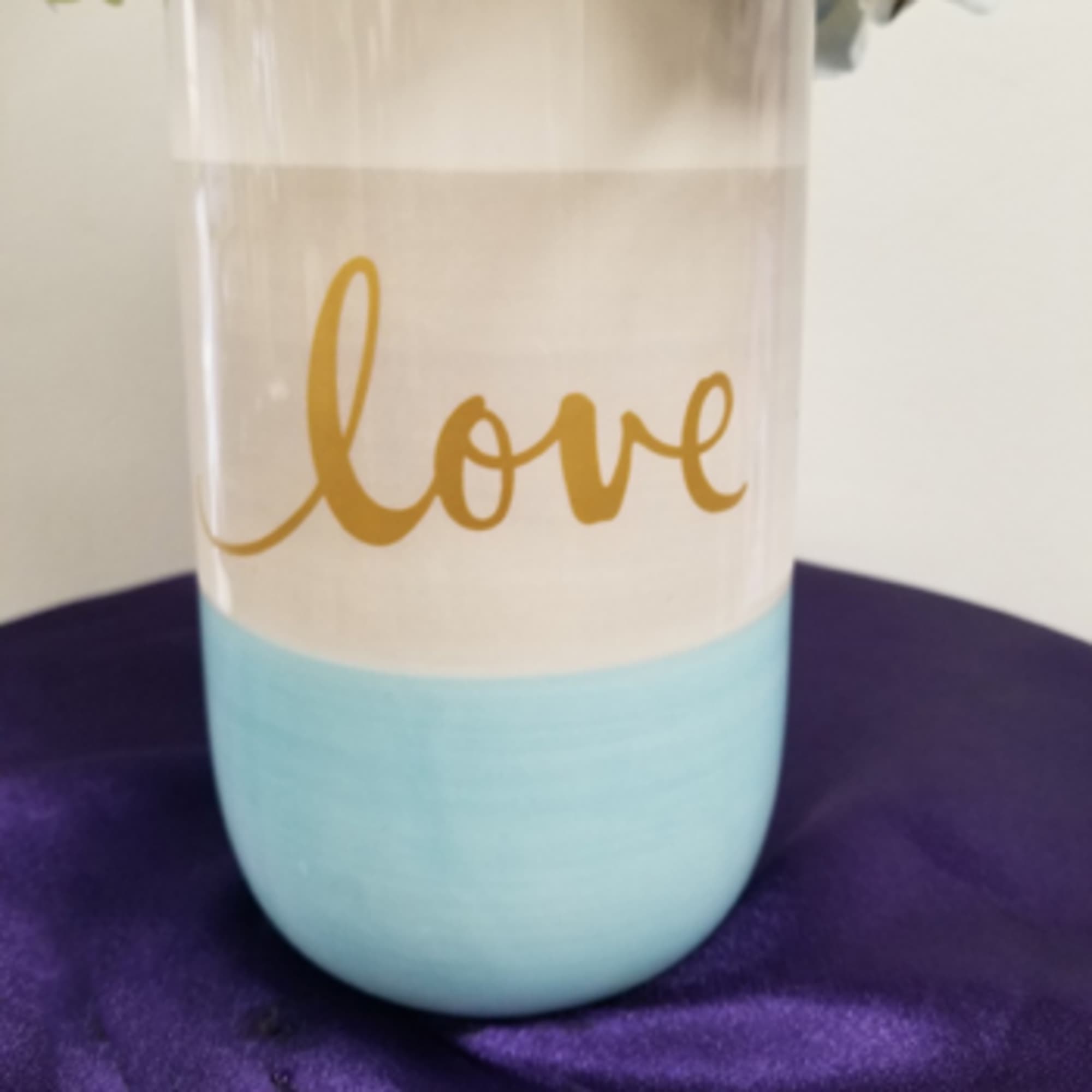 A clear tumbler with gold "love" lettering and a light blue base