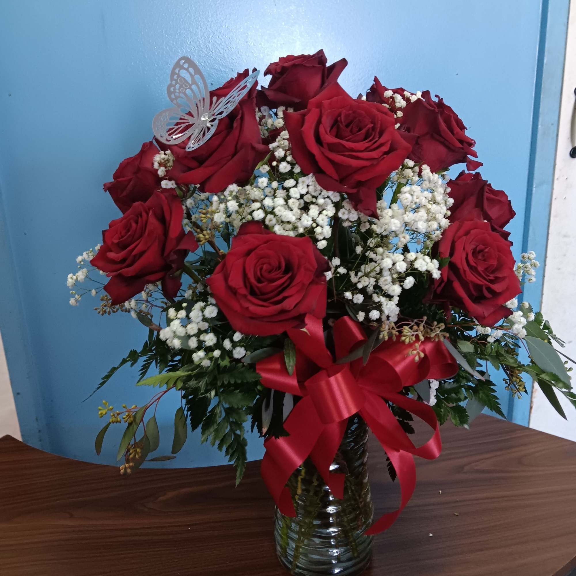 Red roses arranged in a glass vase with white baby's breath and a red ribbon