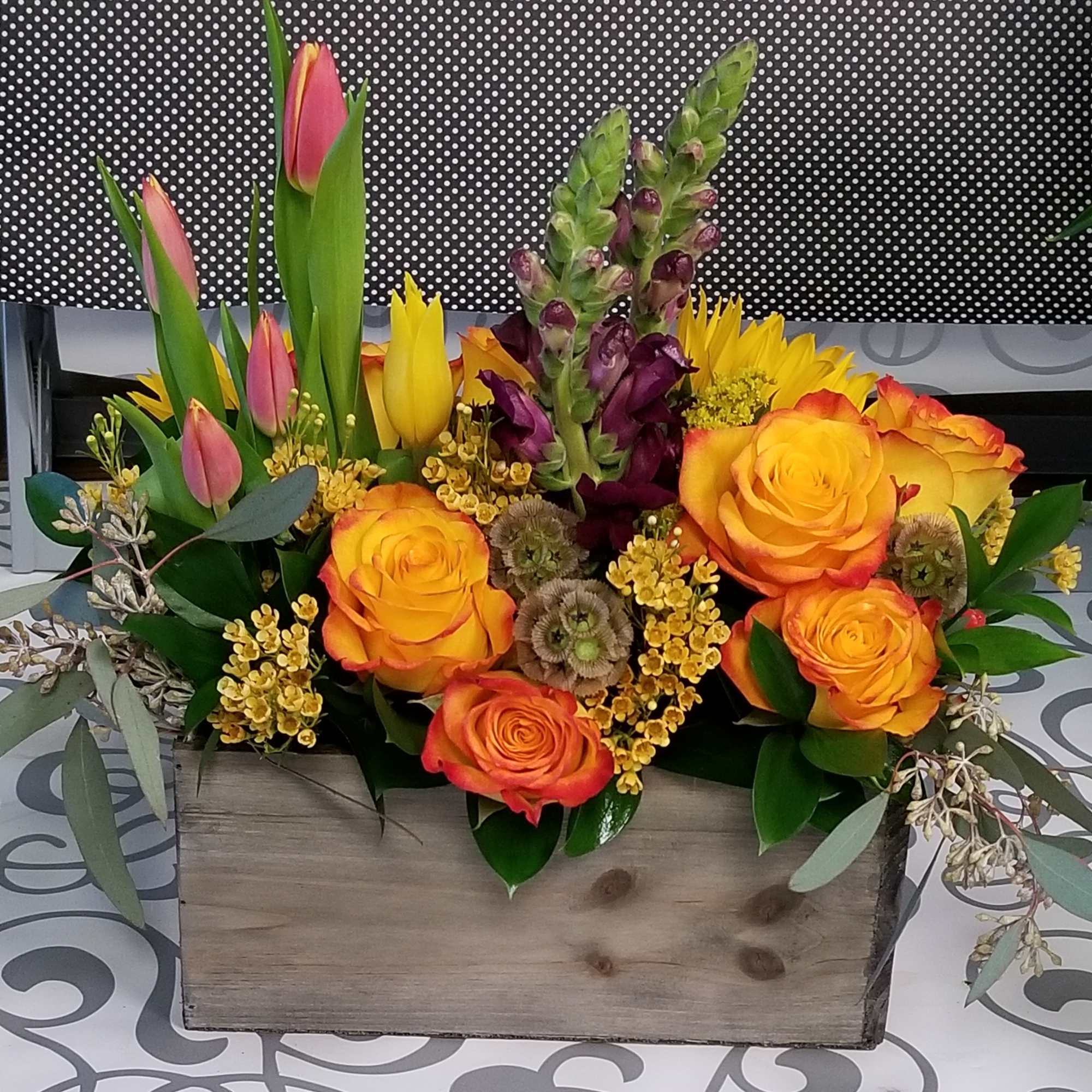 Mixed bouquet of orange roses, pink tulips, and purple blooms in a wooden box