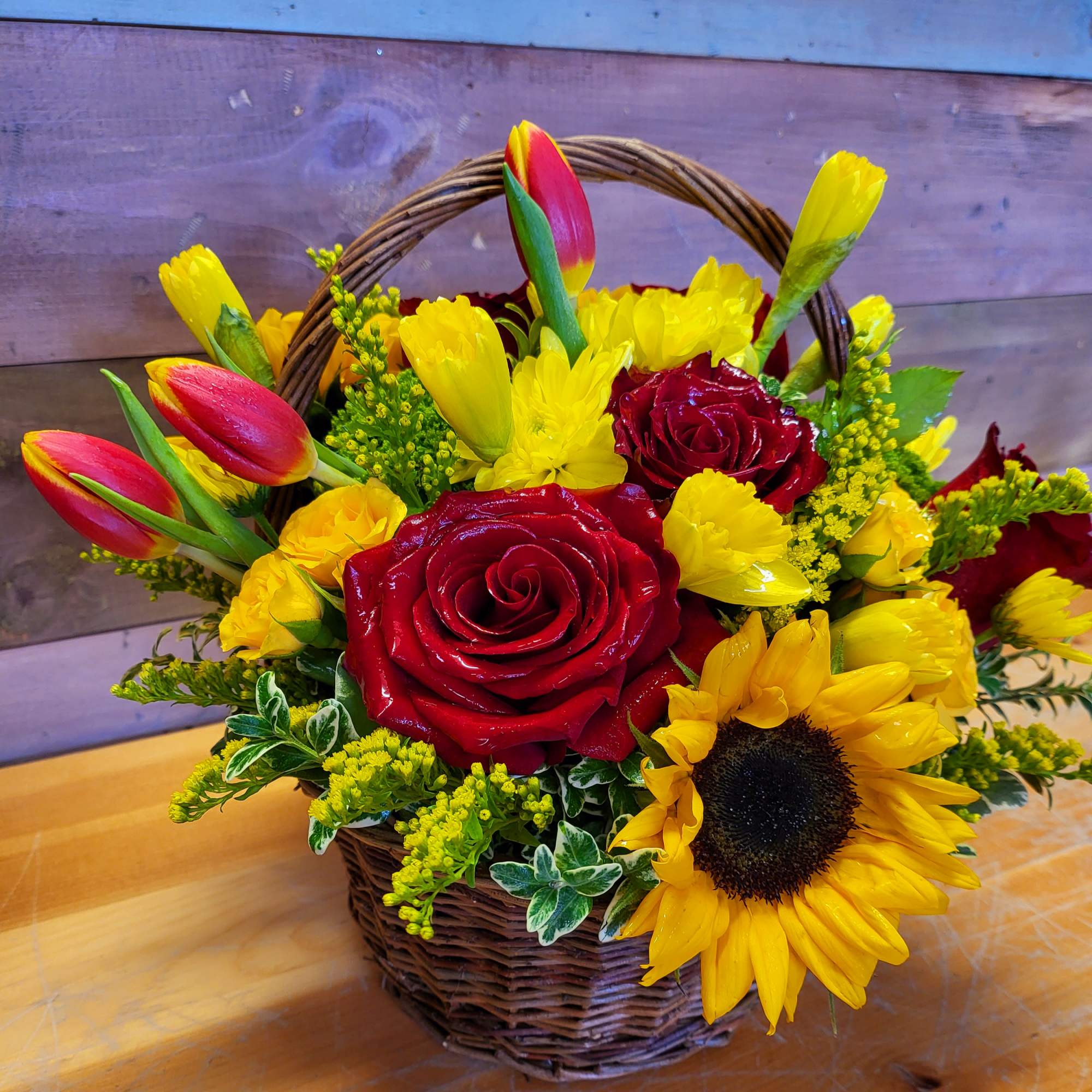 Basket arrangement with red roses, yellow tulips, and a sunflower