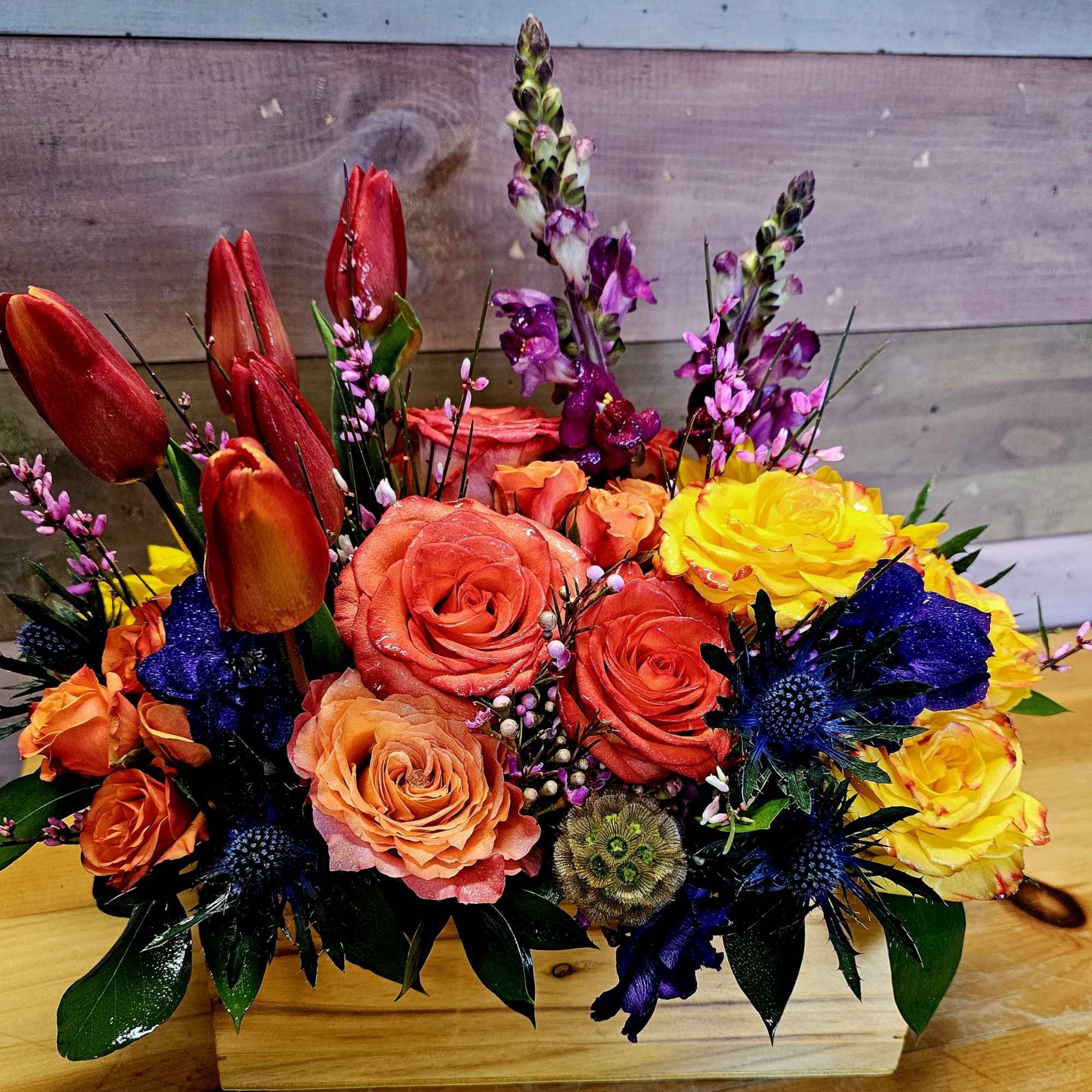 Colorful bouquet with roses, tulips, and purple accent flowers in a wooden box