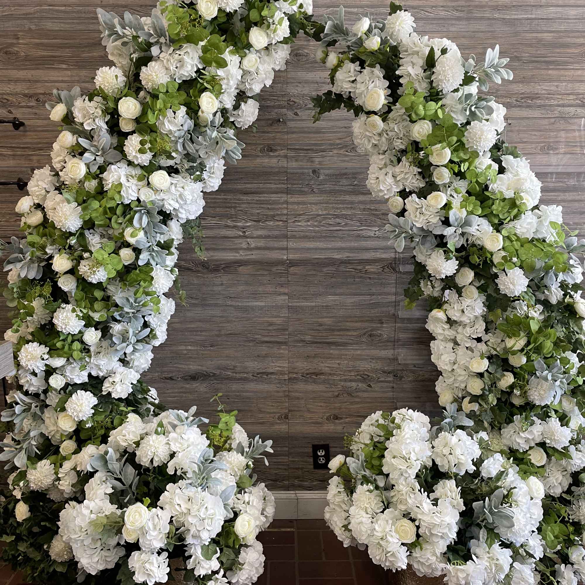 Large white floral arch with green accents in gold pots