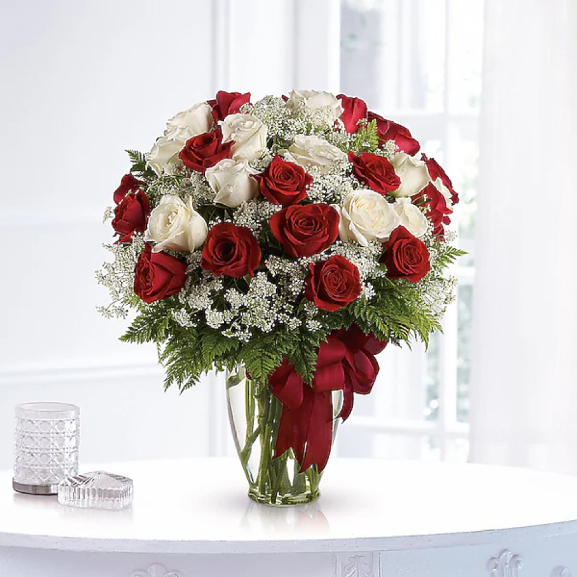 Red and white roses arranged in a clear glass vase with a red ribbon
