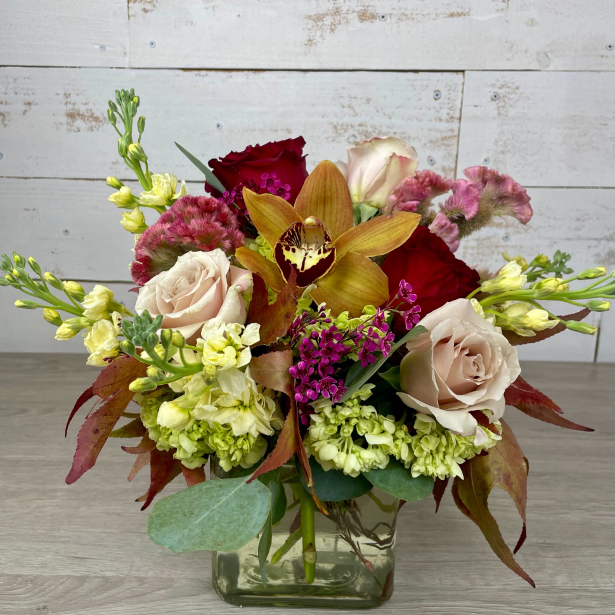 Mixed bouquet in a square glass vase with roses and an orchid