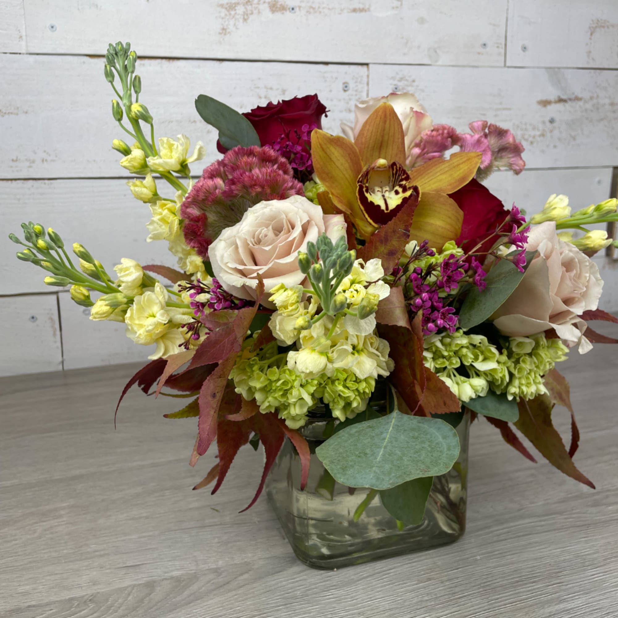 Mixed bouquet in a square glass vase with roses, orchids, and green hydrangeas