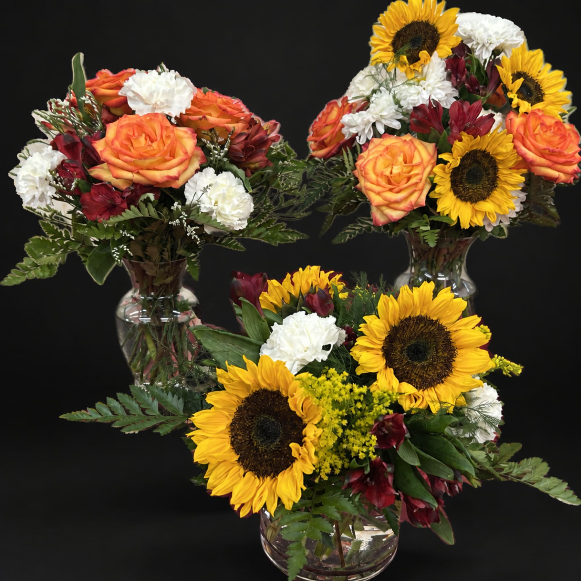 Three mixed flower arrangements with sunflowers, roses, and carnations in glass vases