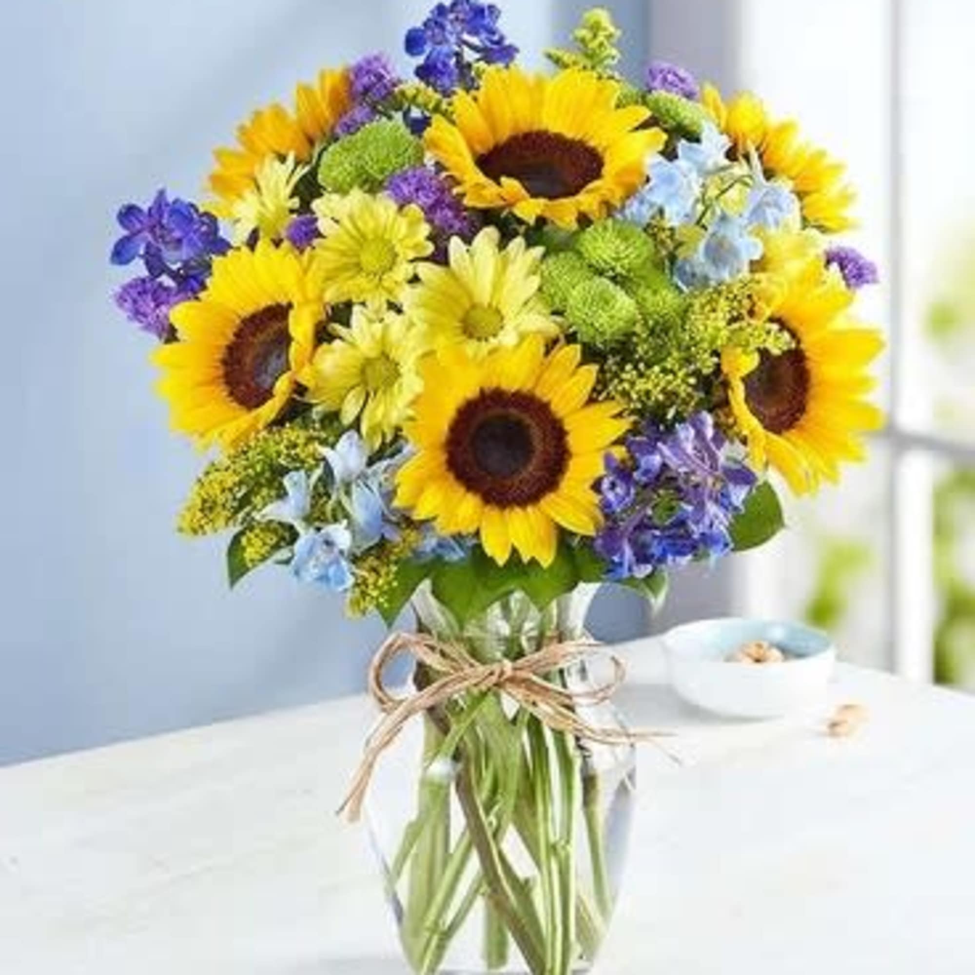 Bouquet of sunflowers, purple flowers, and blue blooms in a glass vase
