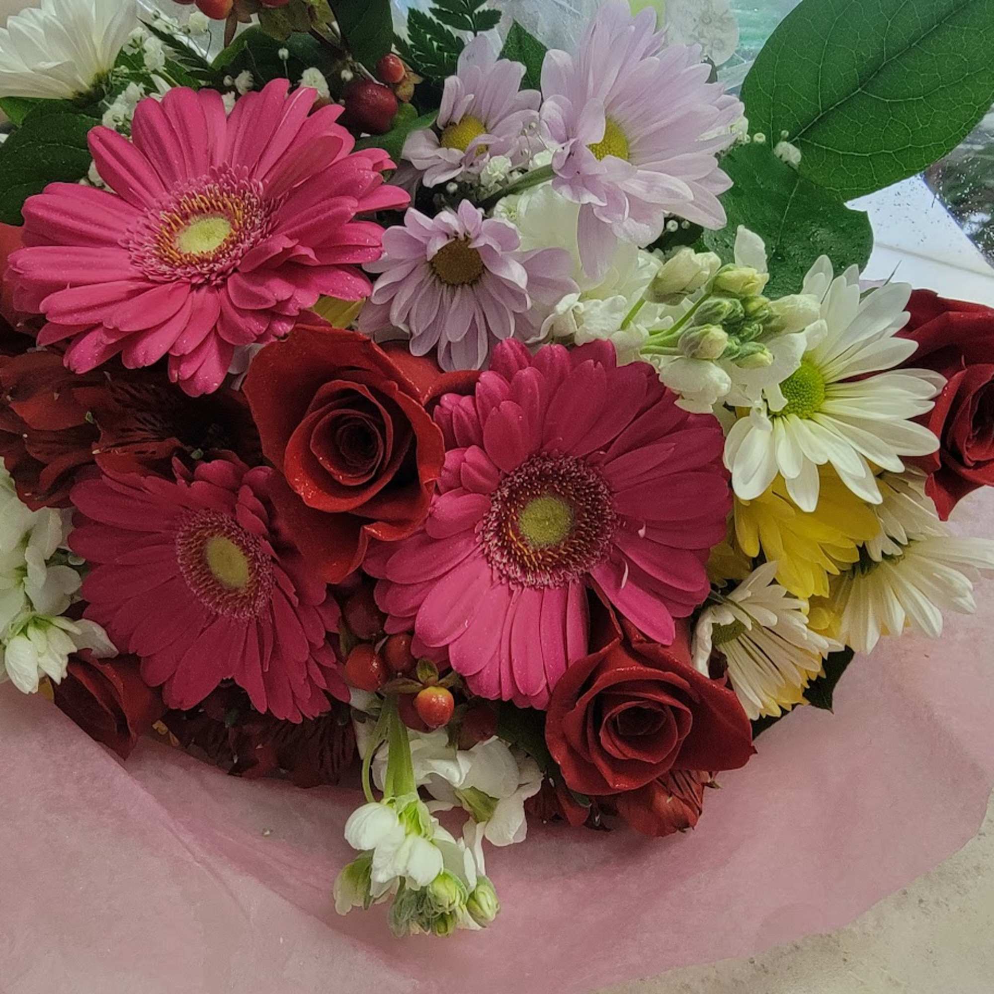 Bouquet of pink gerbera daisies, red roses, and white daisies wrapped in pink paper