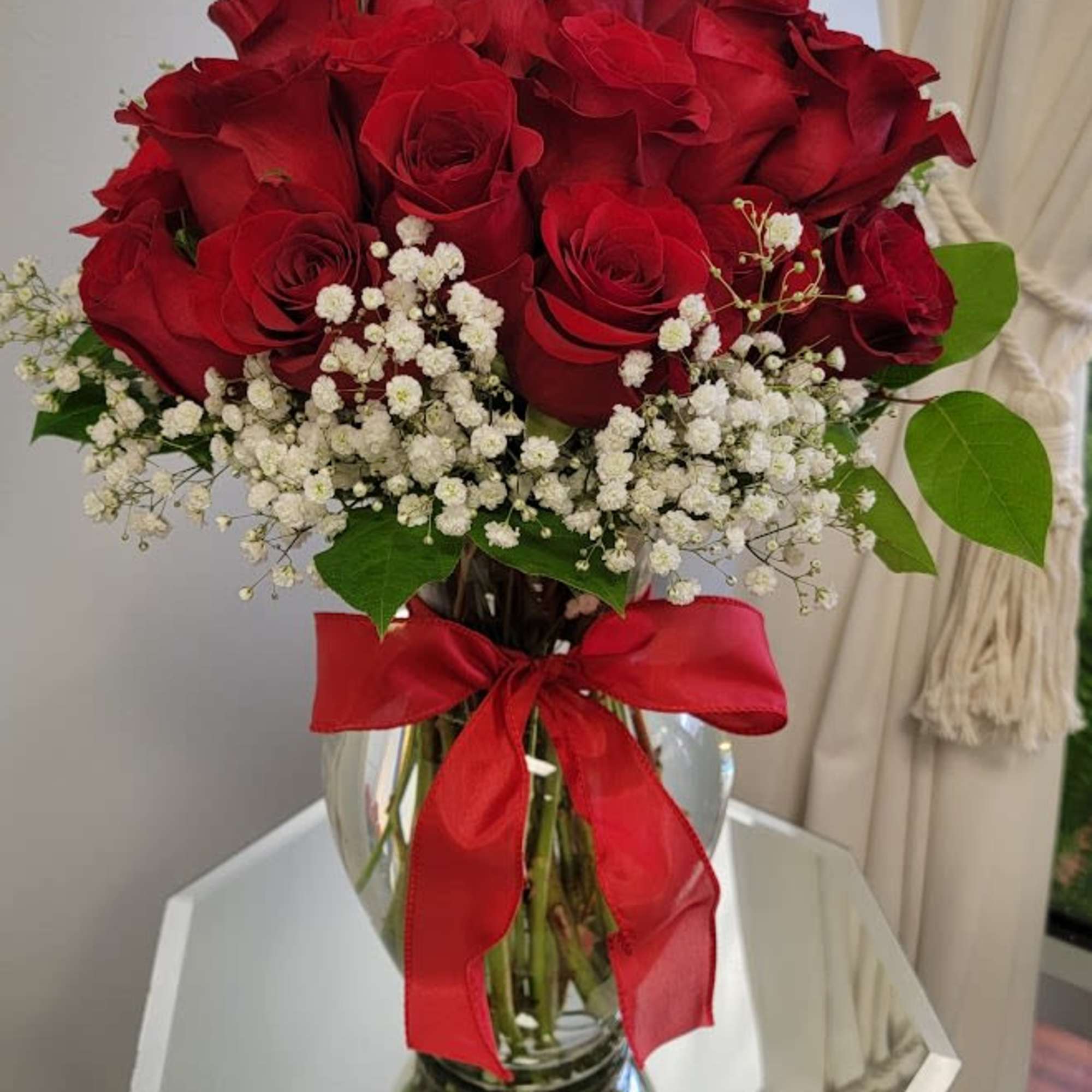 Red roses in a glass vase with white baby's breath and a red ribbon