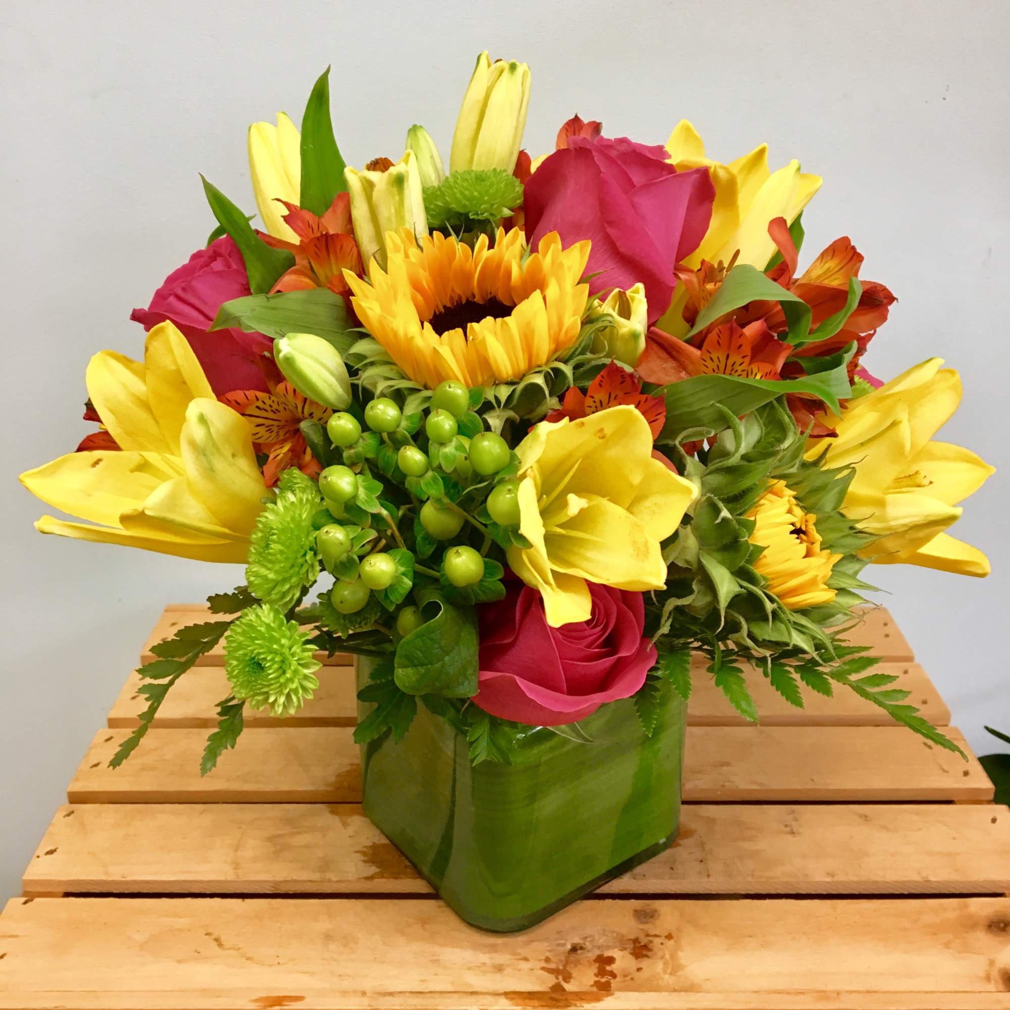 Bright mixed bouquet with sunflowers, yellow lilies, and pink roses in a green vase