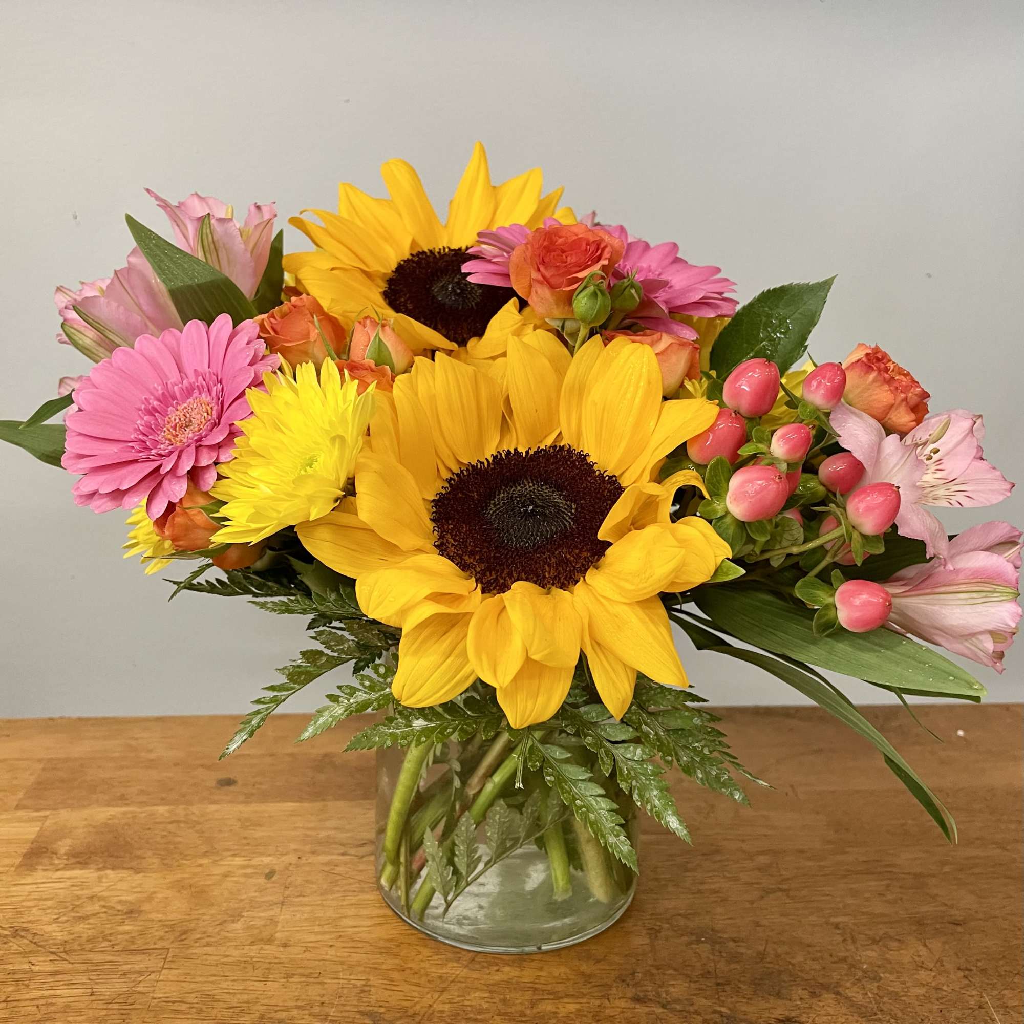 Mixed bouquet with sunflowers, pink gerberas, and roses in a glass vase