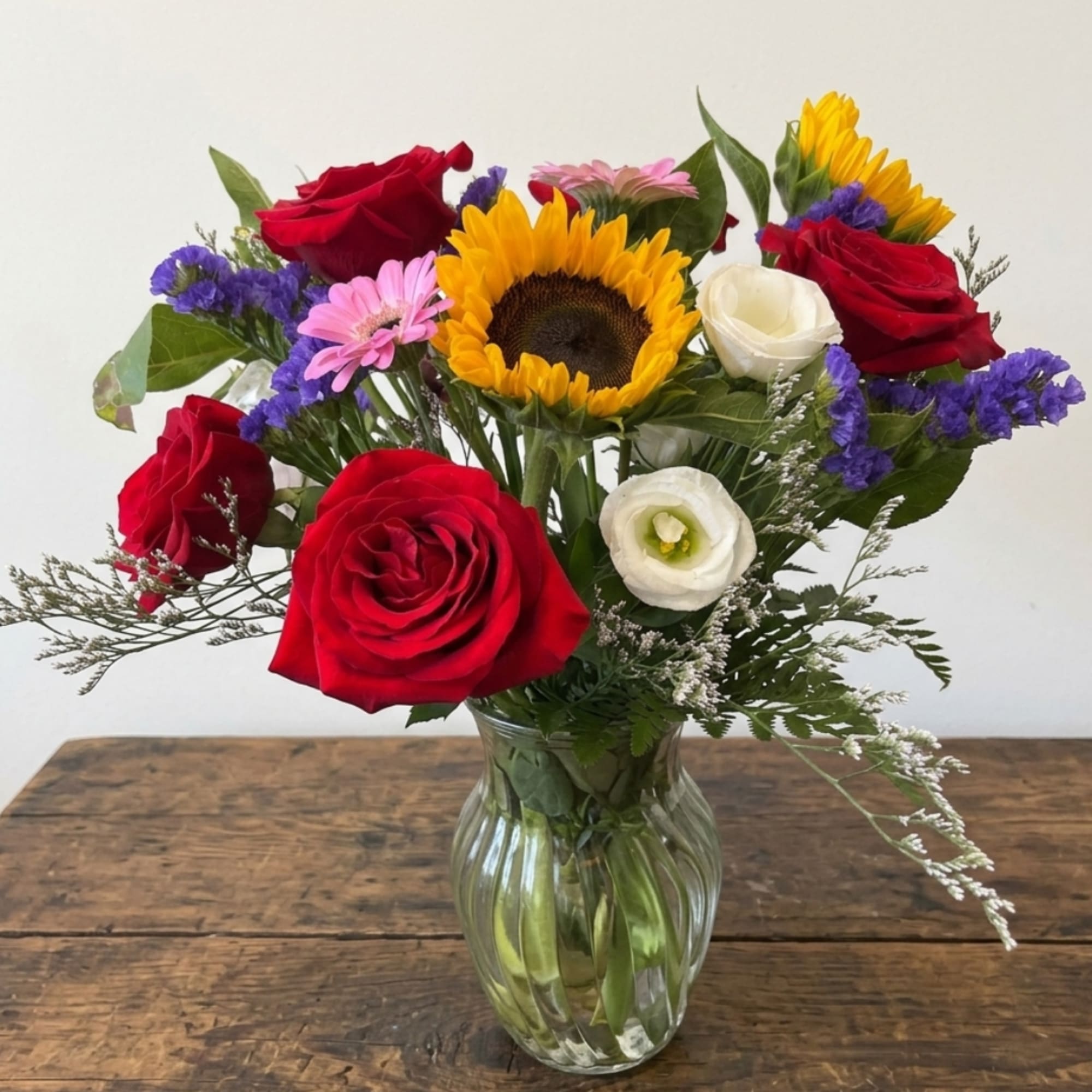 Mixed bouquet with red roses, a sunflower, and white blooms in a glass vase