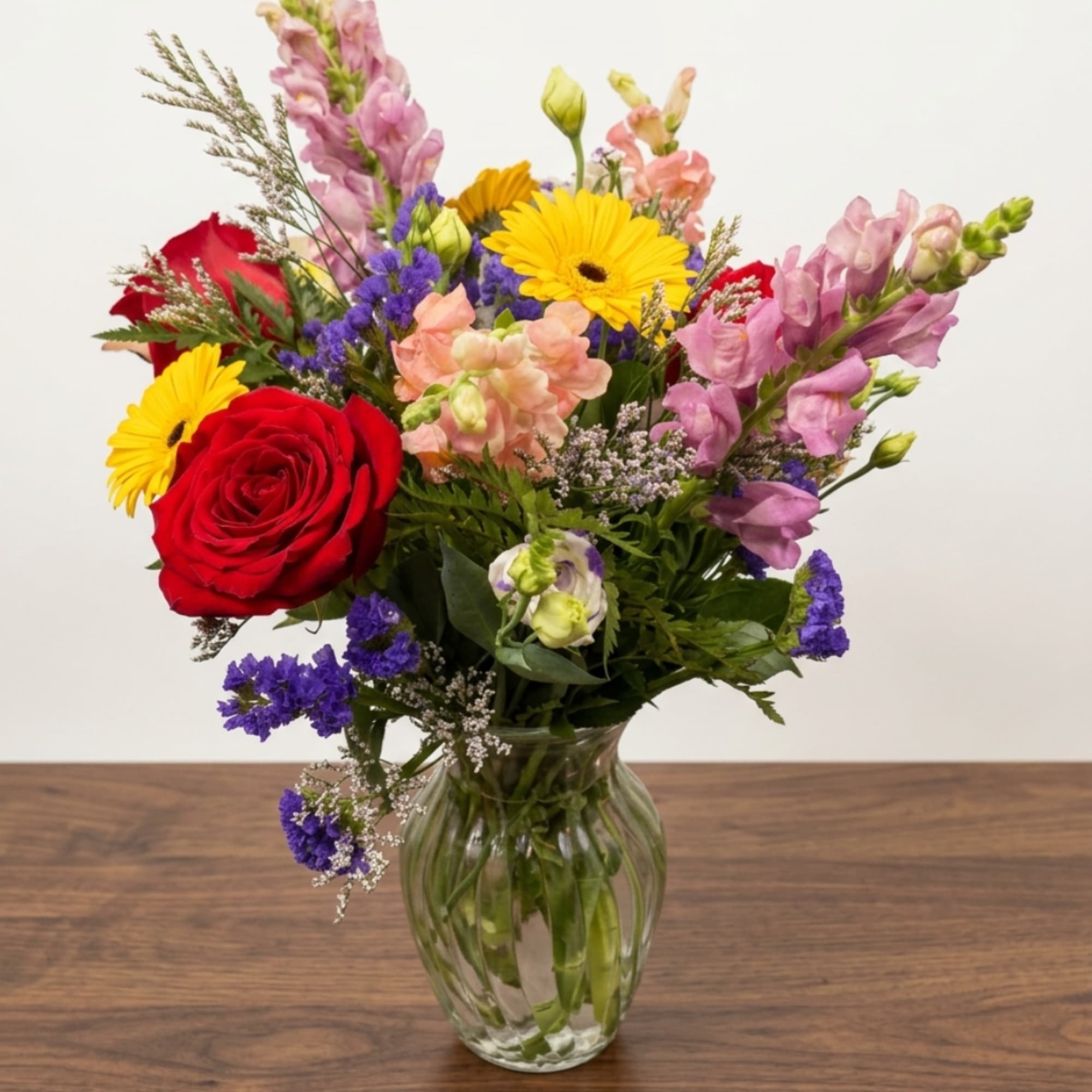 Mixed bouquet of roses, gerbera daisies, and snapdragons in a glass vase