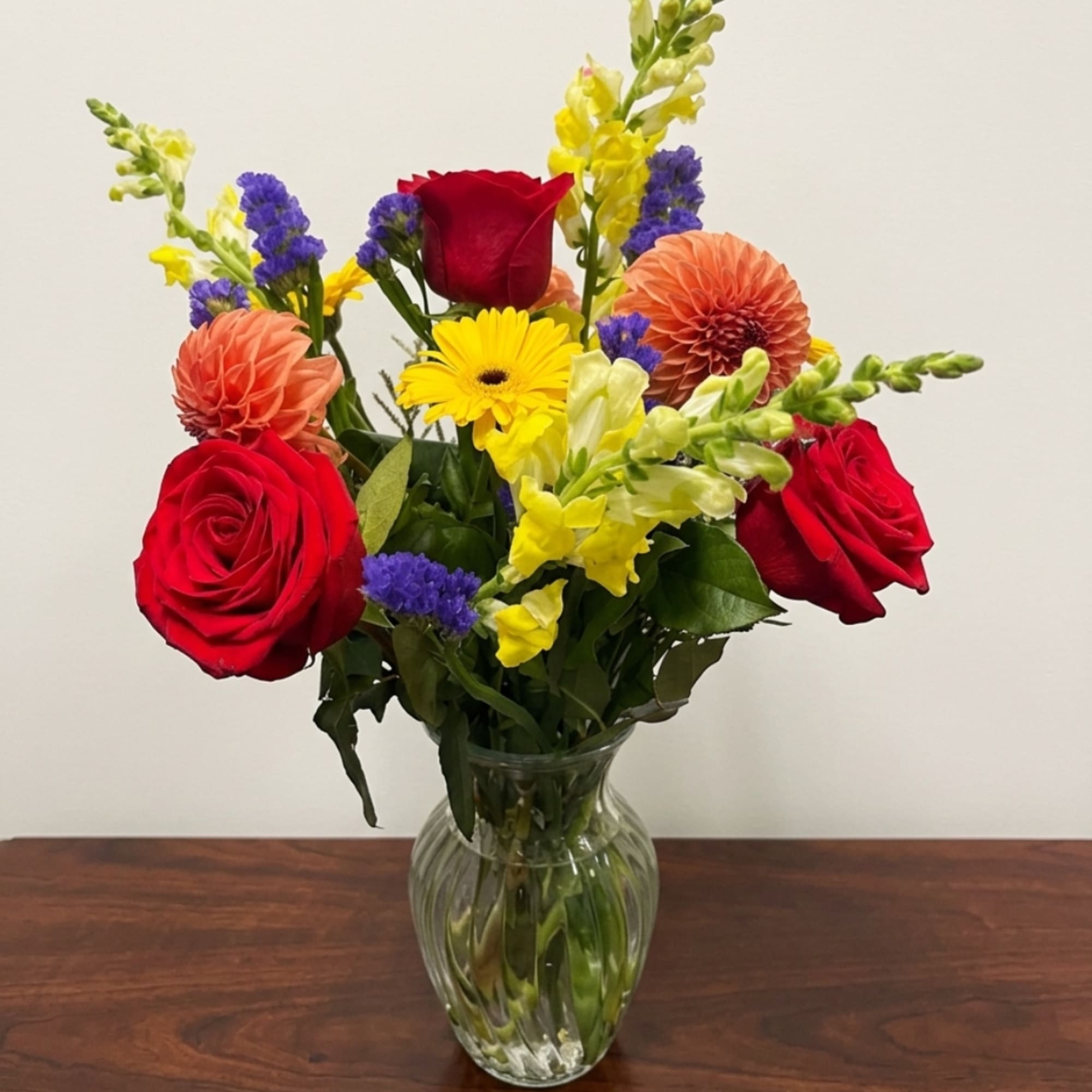 Mixed bouquet of red roses, yellow daisies, and orange dahlias in a clear glass vase